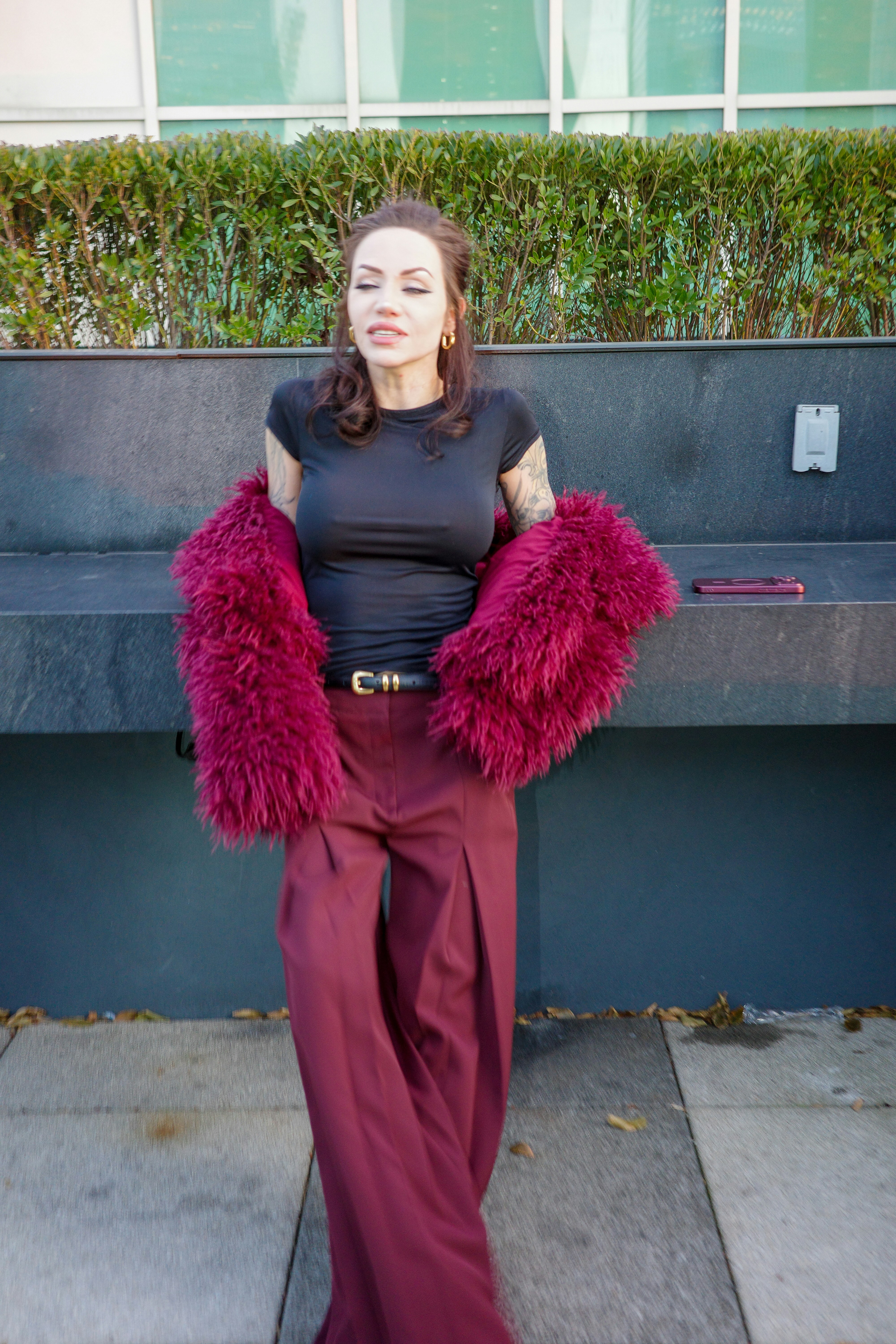 A woman in a black t-shirt and burgundy trousers with a faux fur coat