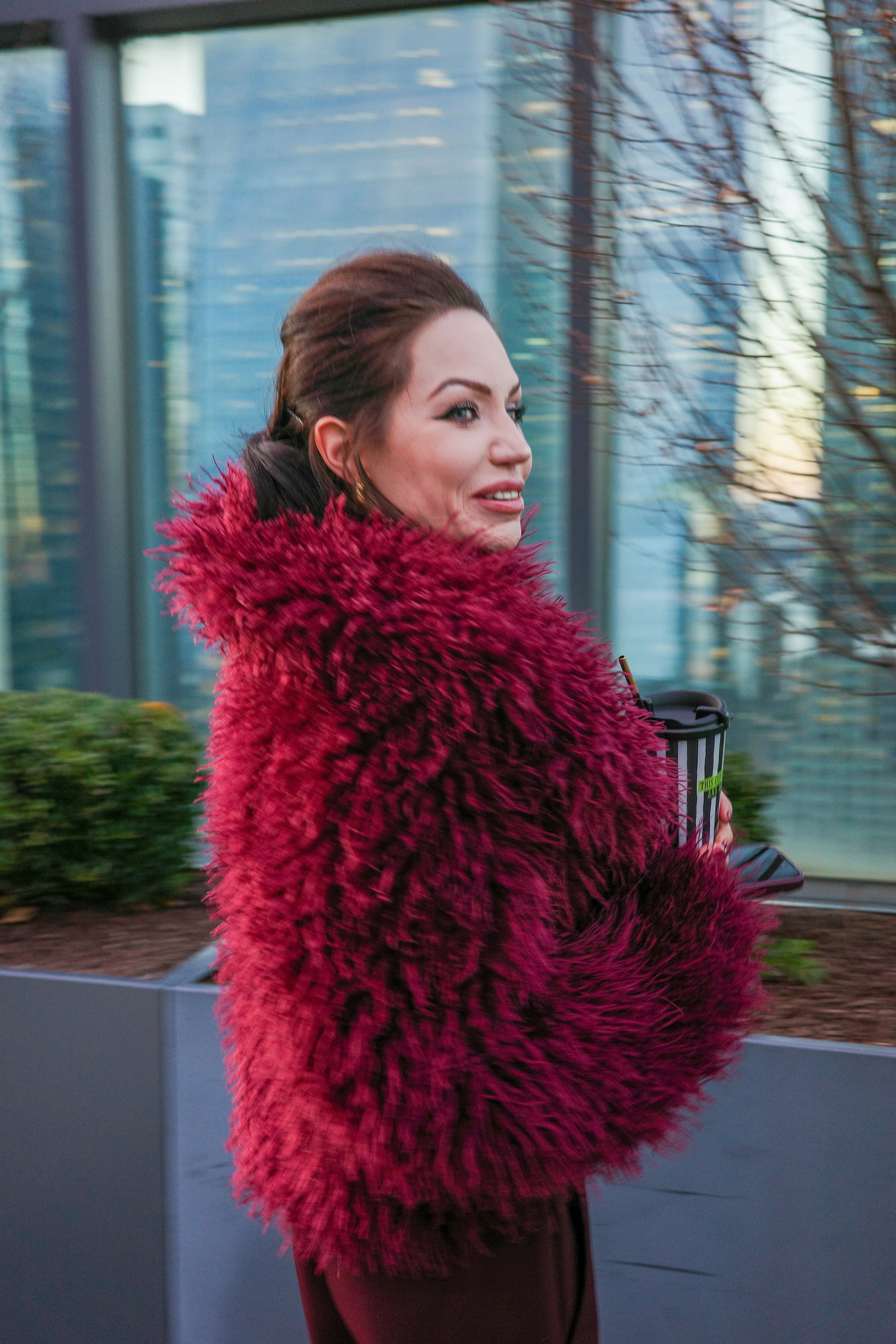A woman in a burgundy faux fur coat holding a striped coffee cup
