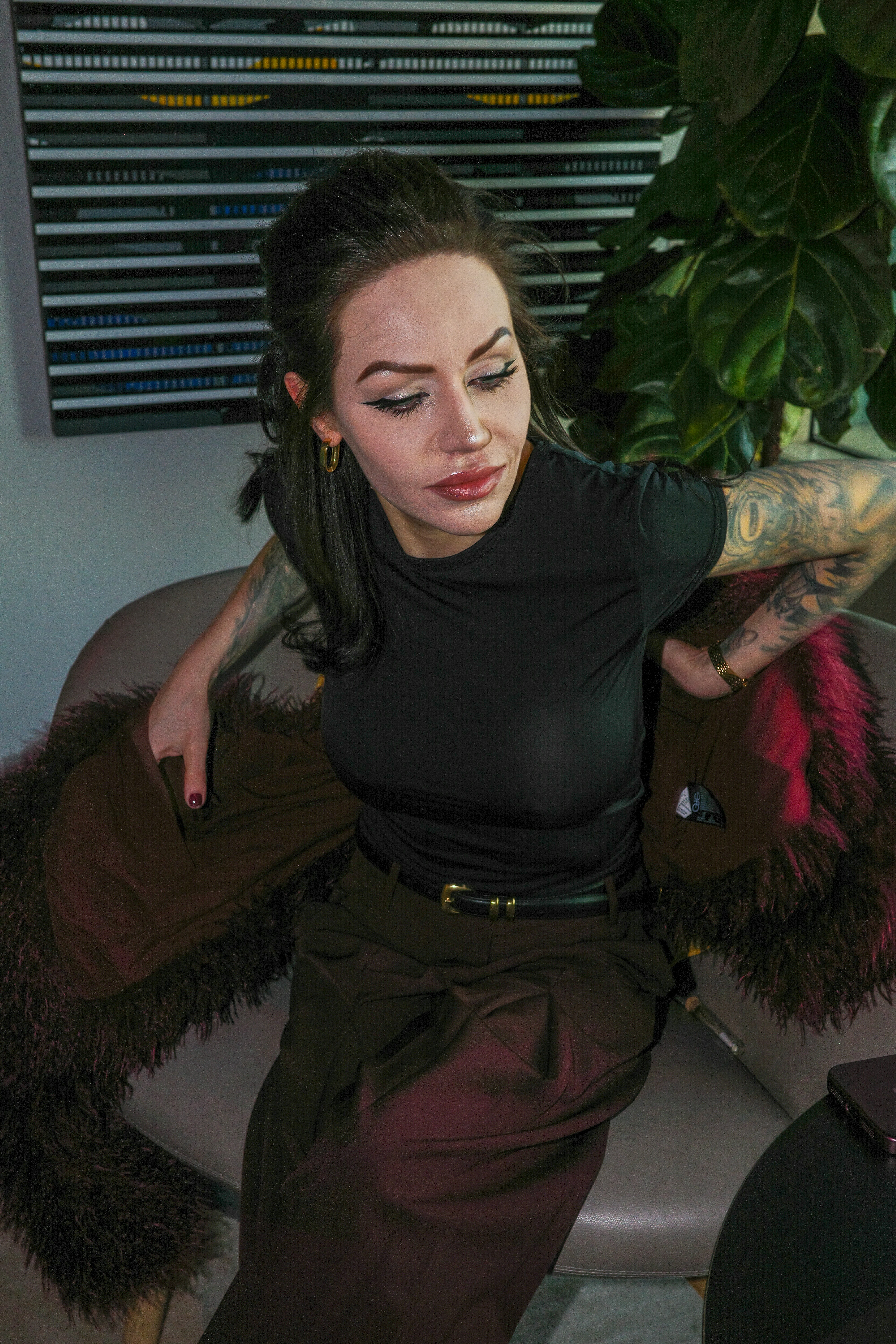 A woman with arm tattoos putting on a brown faux fur coat