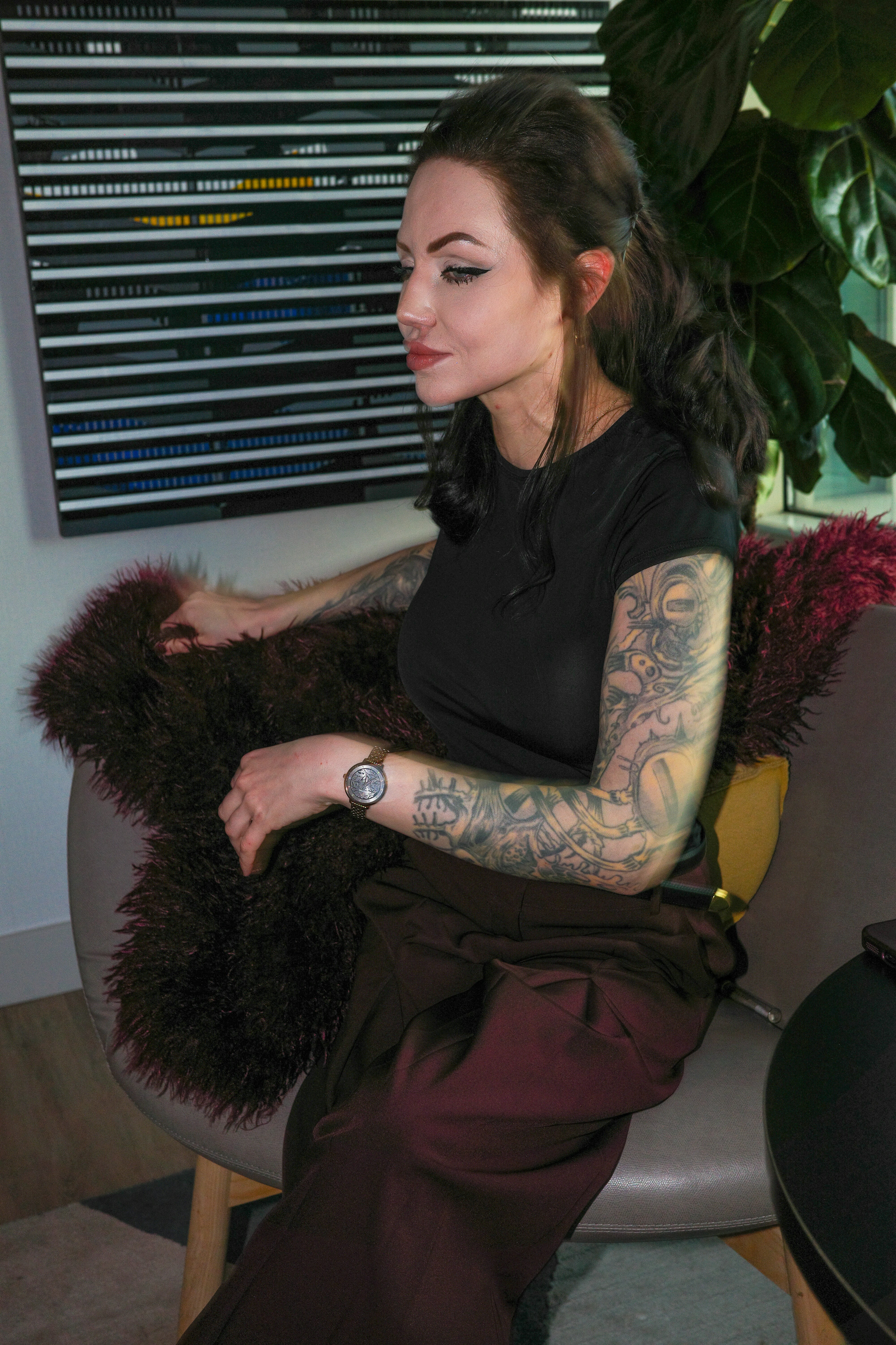 A woman with arm tattoos in a black t-shirt sitting on a chair
