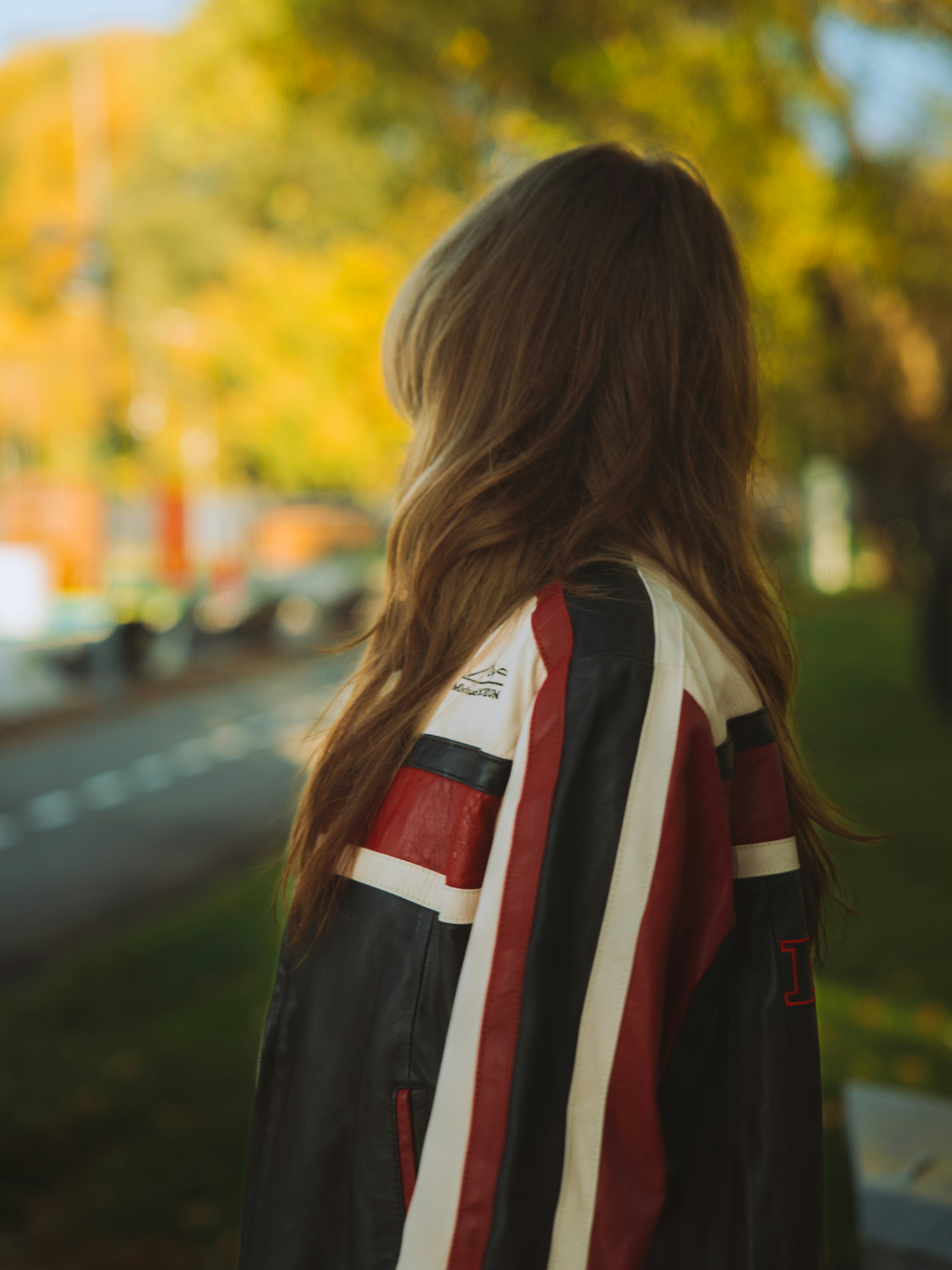 A person with long brown hair wearing a black, red, and white leather jacket