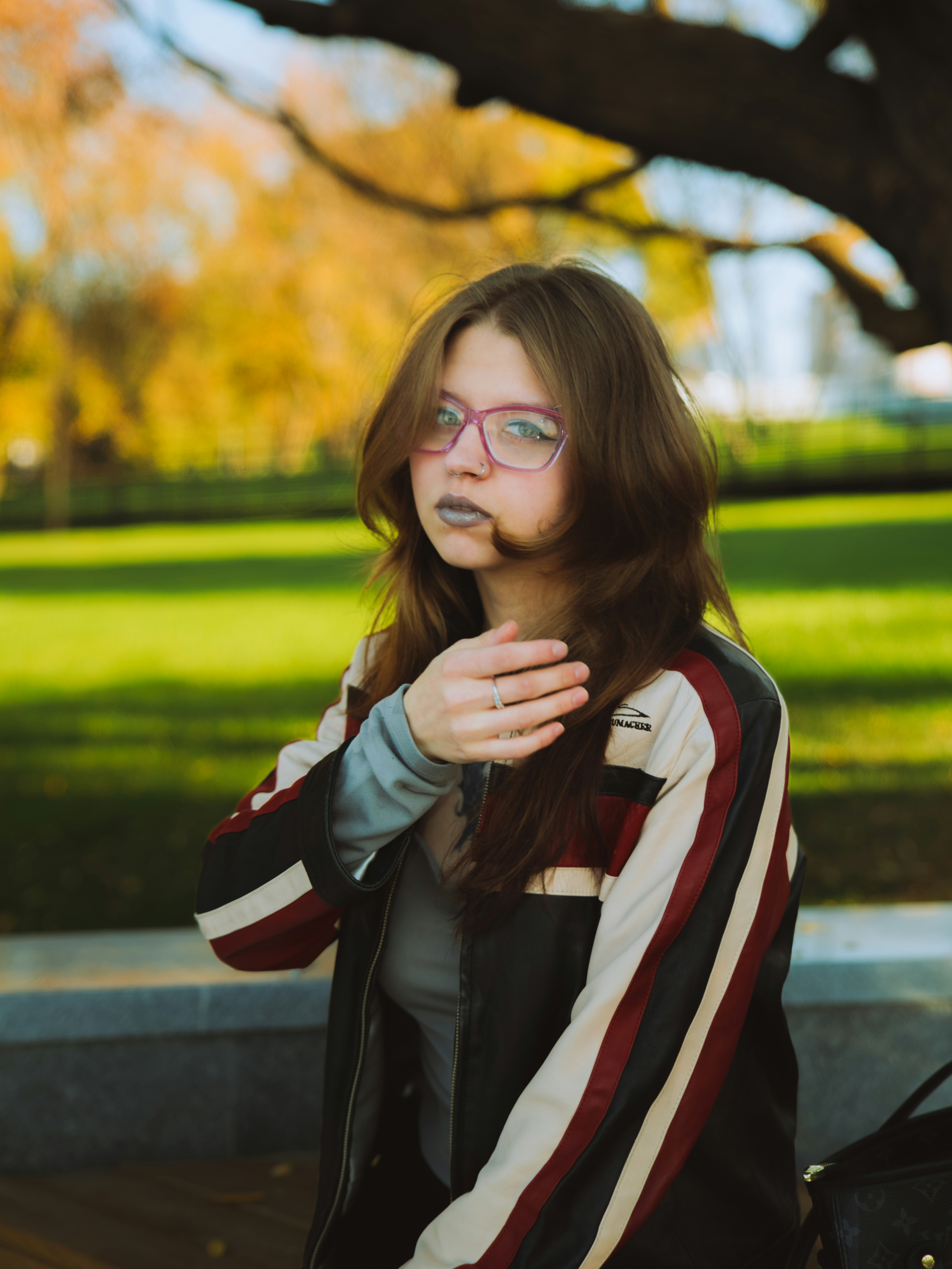 A woman with pink glasses and dark lipstick in a striped leather jacket