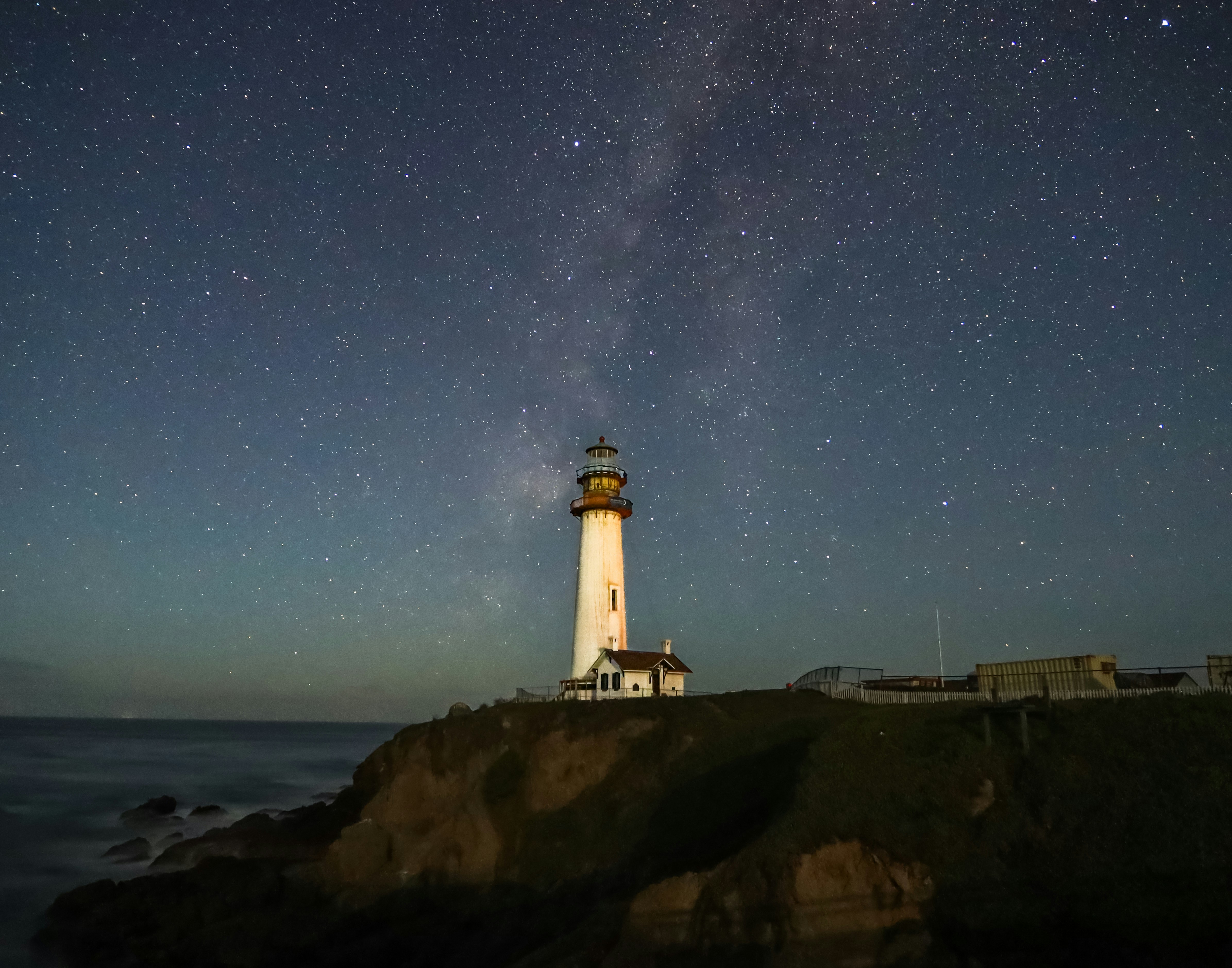 A lighthouse on a rocky cliff under a starry night sky