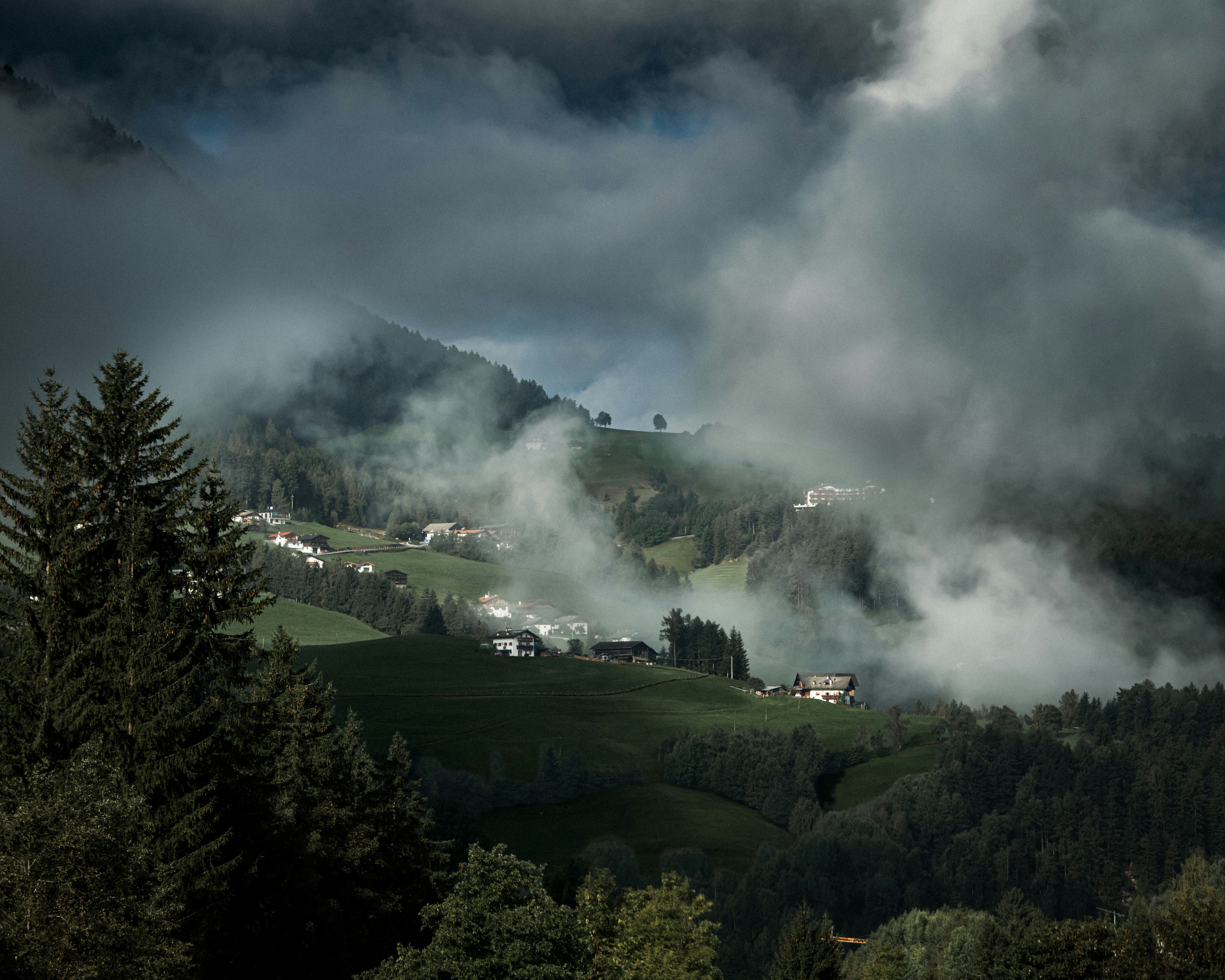 Houses on a green mountain slope partially obscured by thick low clouds