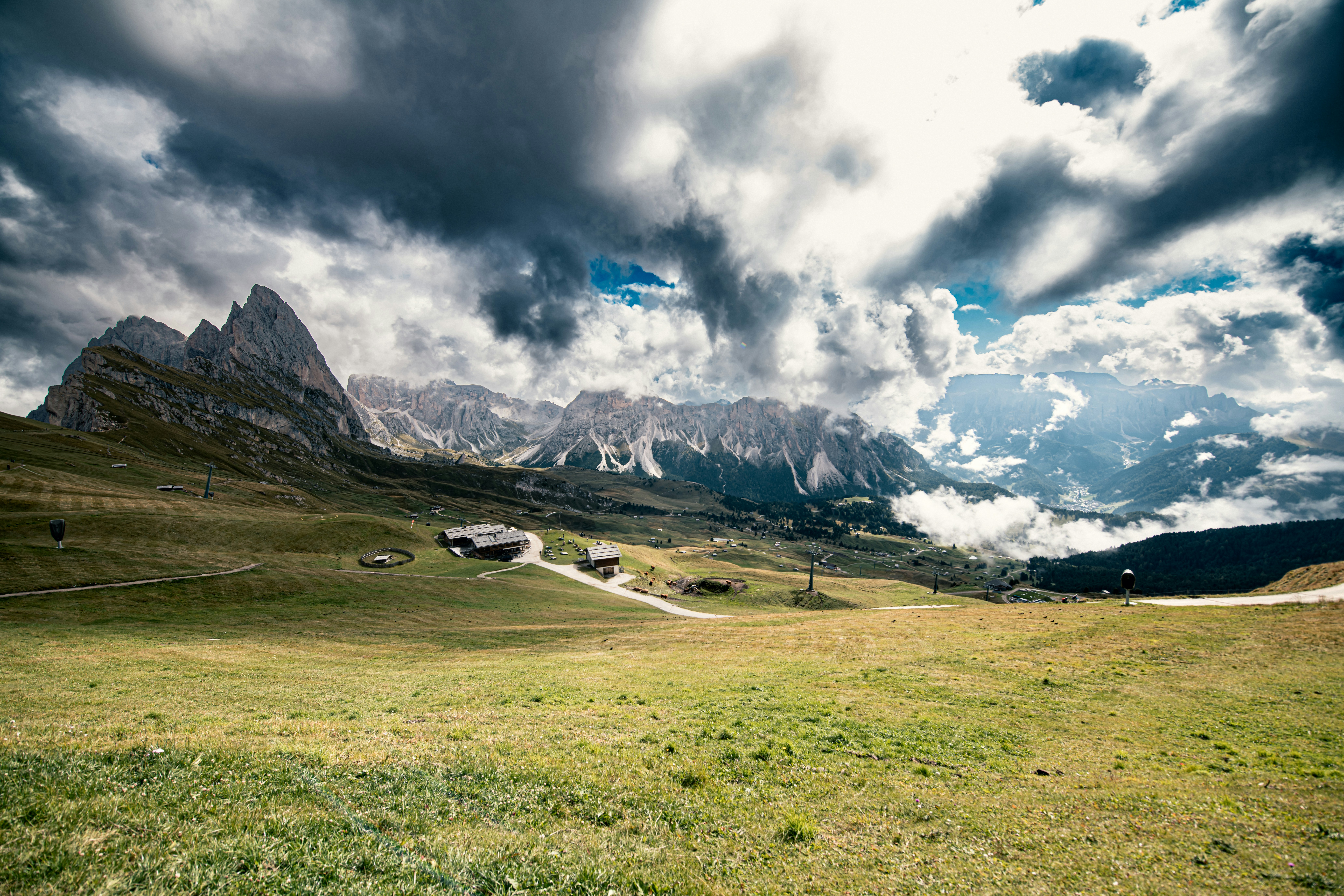 A grassy mountain meadow below the jagged peaks of the Dolomites under stormy clouds