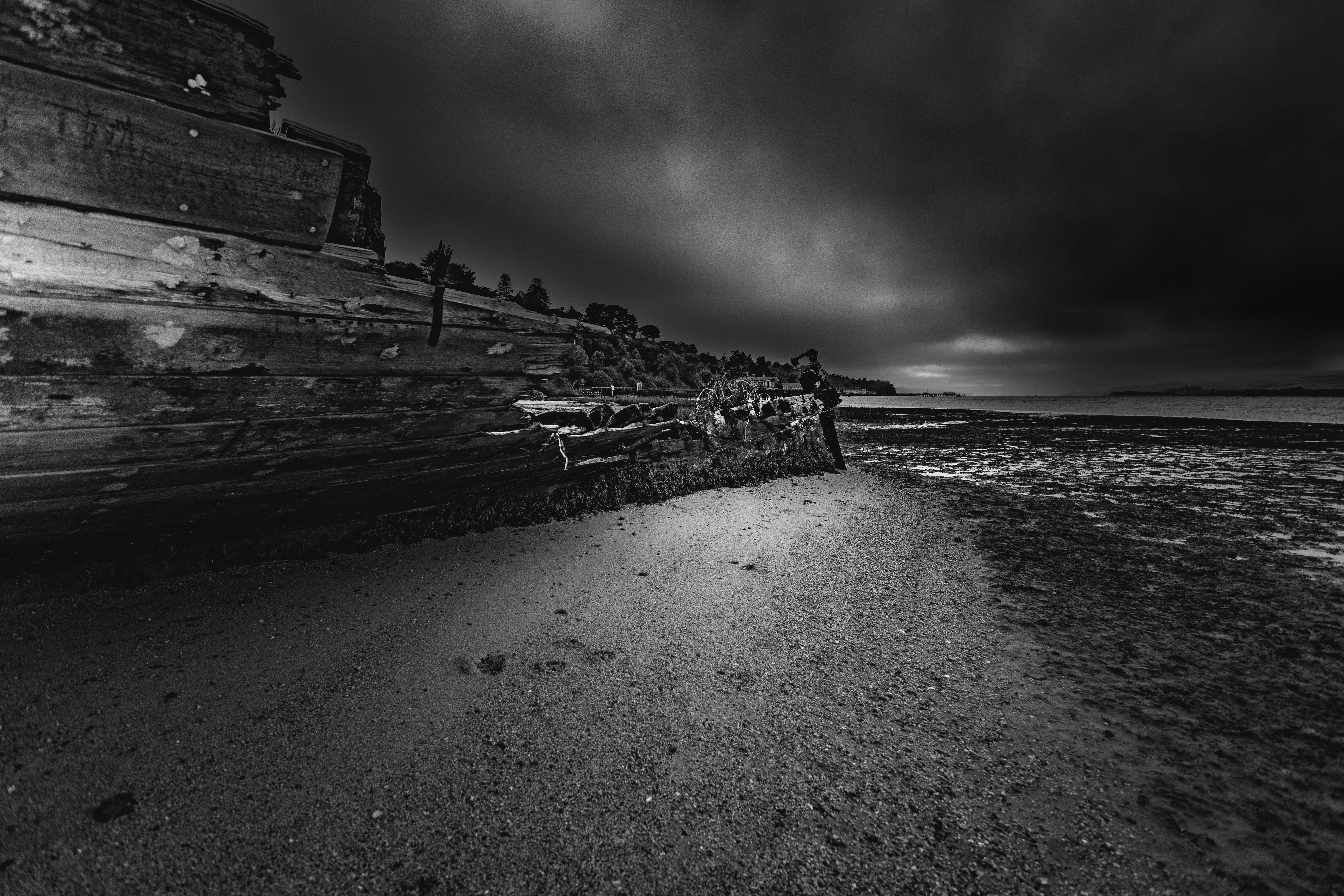 A weathered wooden shipwreck hull on a sandy beach under a dark cloudy sky
