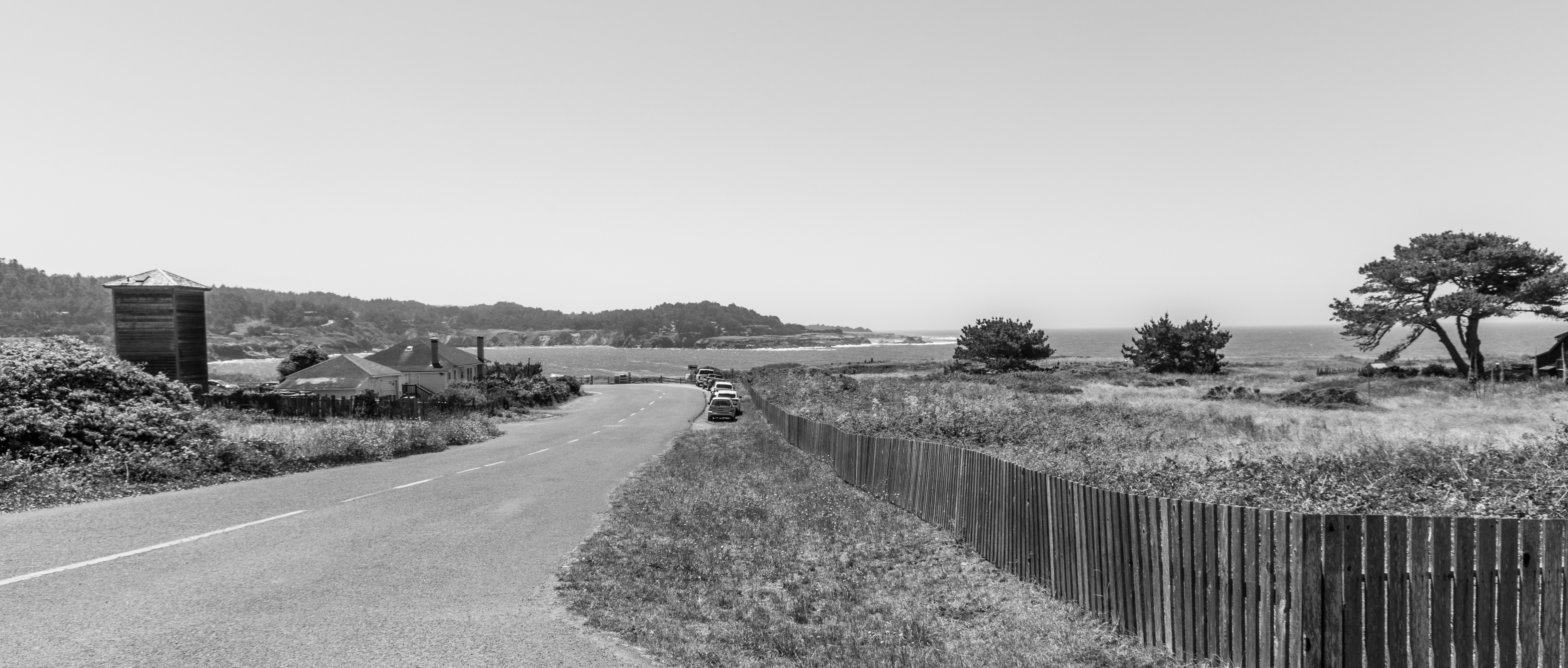A coastal road with a wooden fence and trees overlooking the ocean
