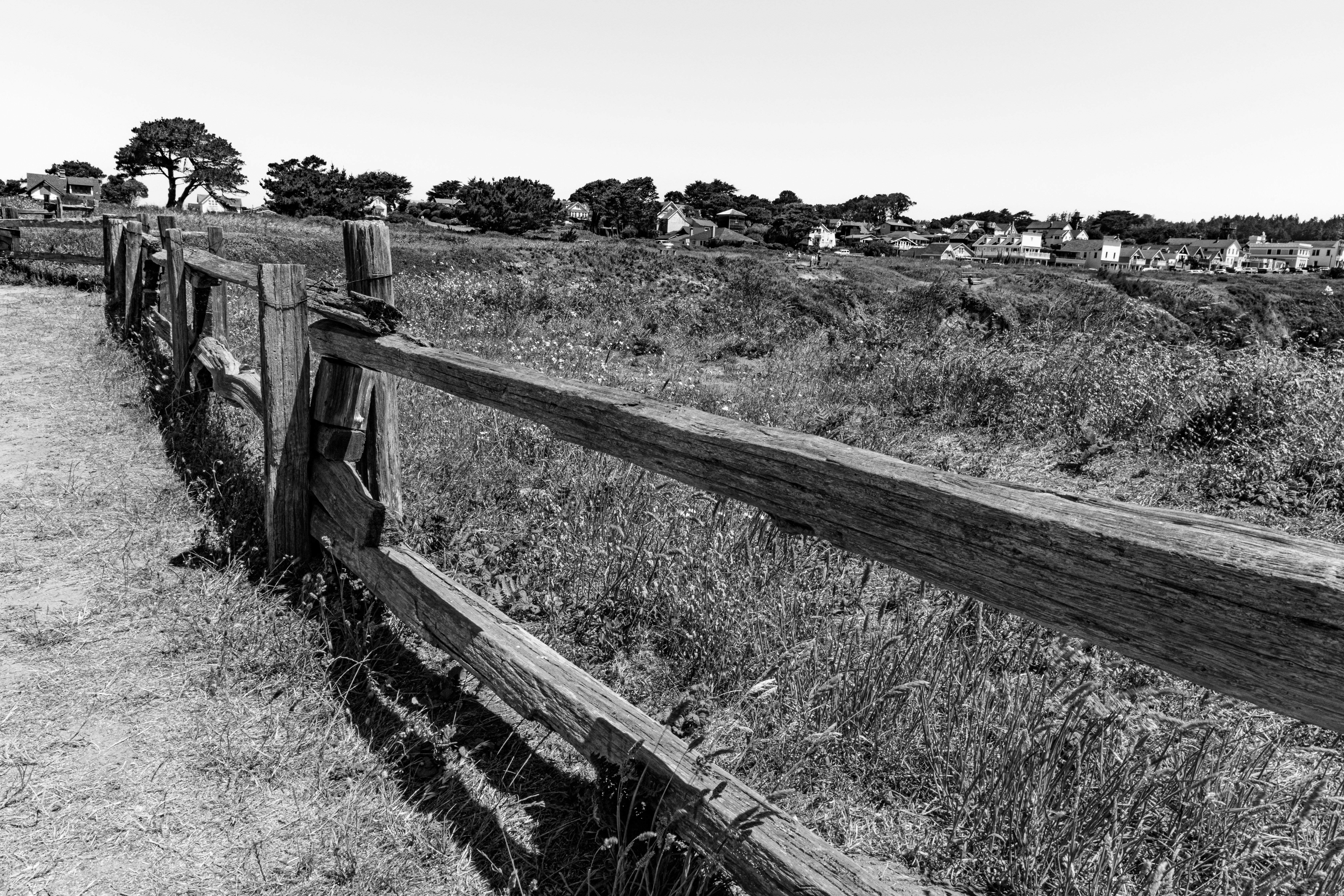 A weathered wooden fence bordering a grassy field with distant houses
