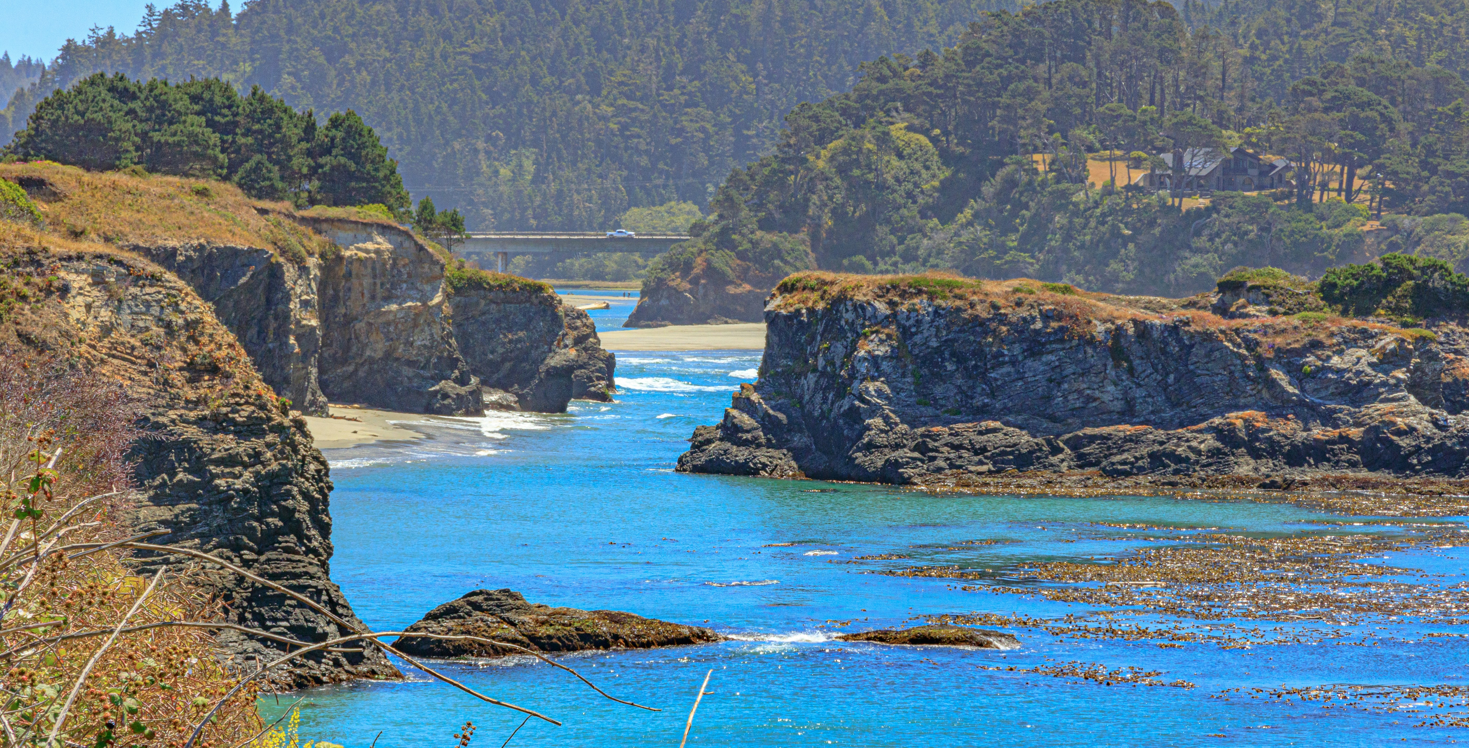 Rocky cliffs framing a blue ocean inlet with a bridge in the distance