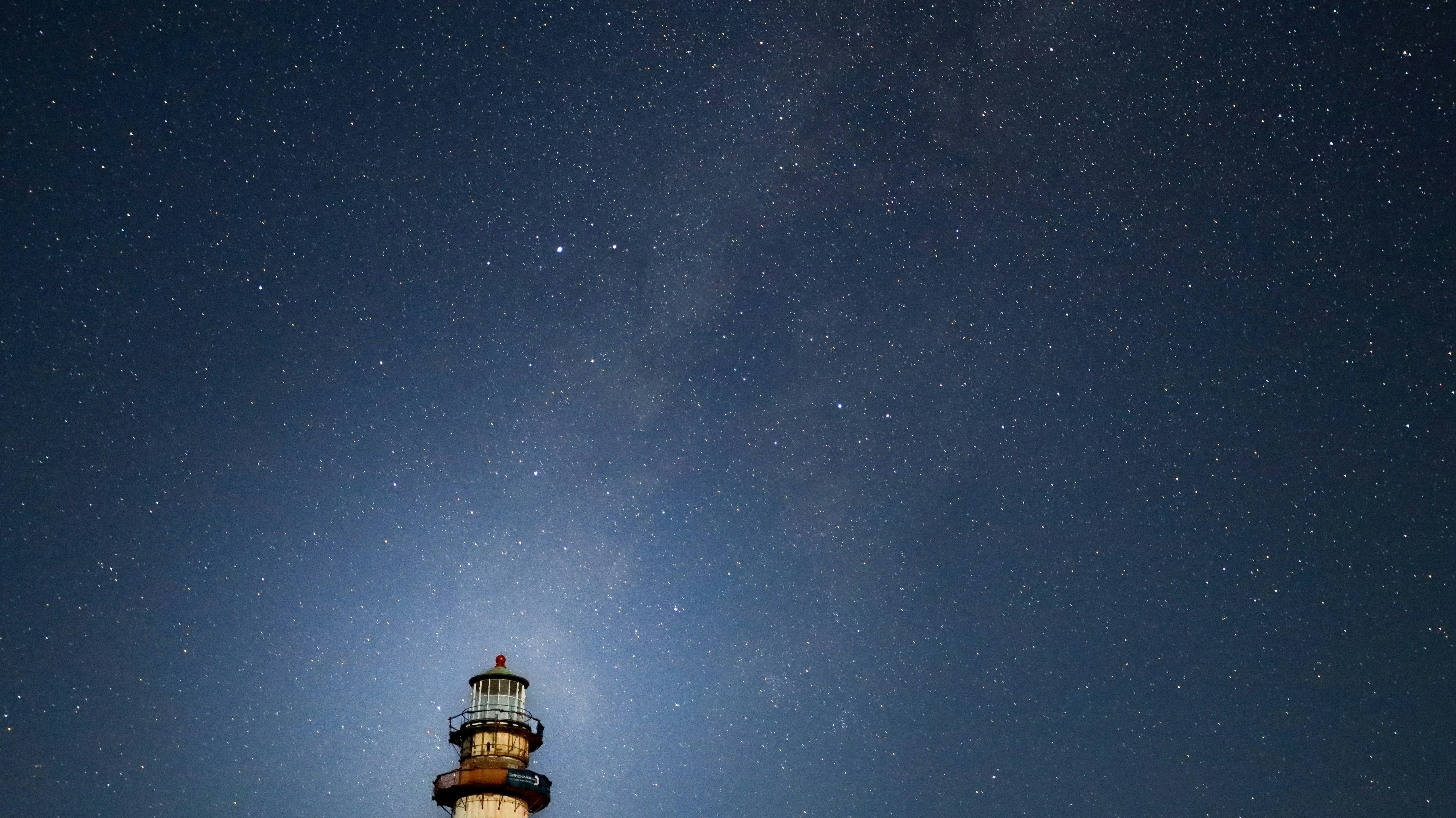 A lighthouse tower illuminated against a vast night sky filled with bright stars