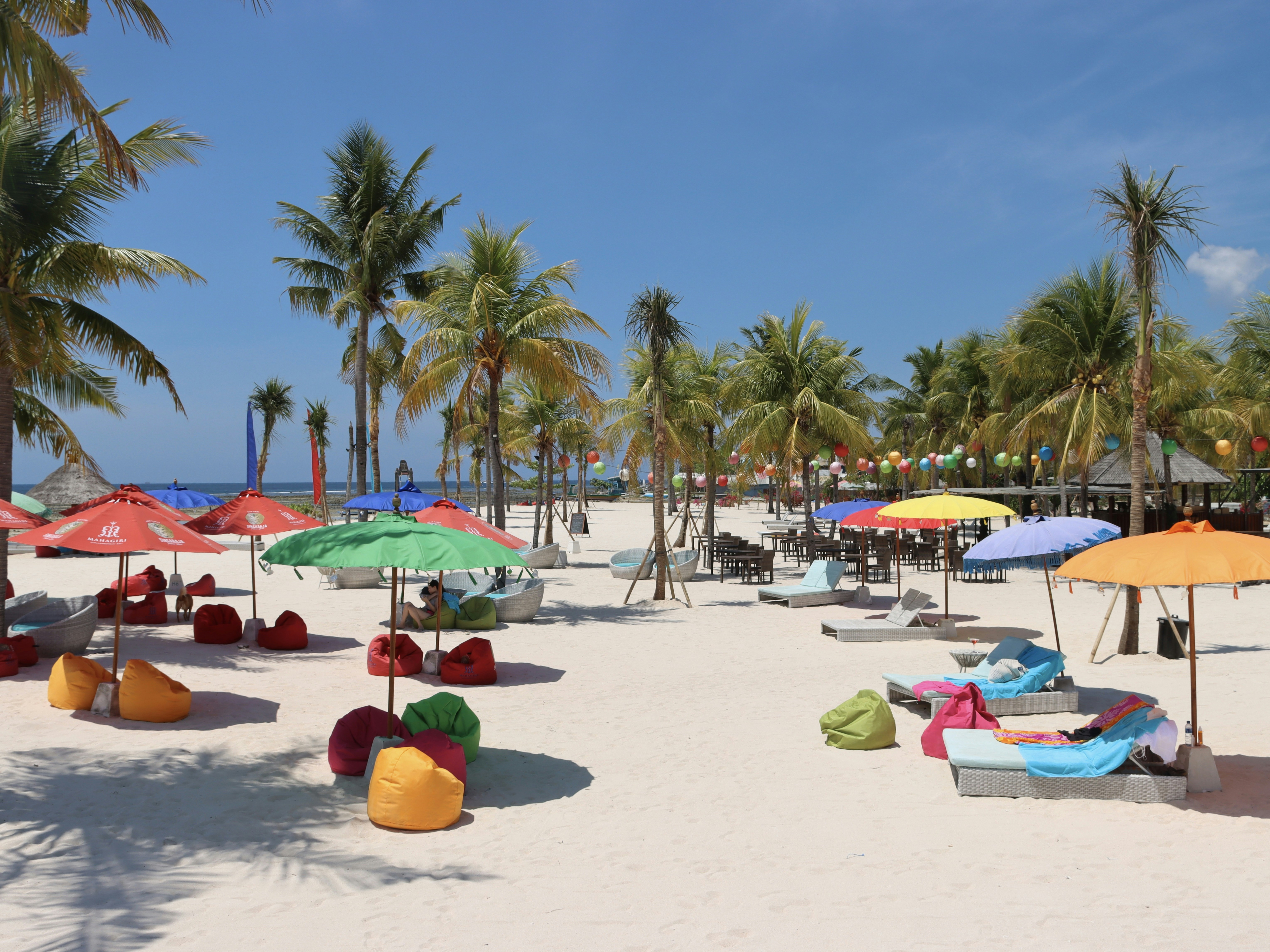 Ombrelli colorati e poltrone a sacco su una spiaggia di sabbia bianca con palme