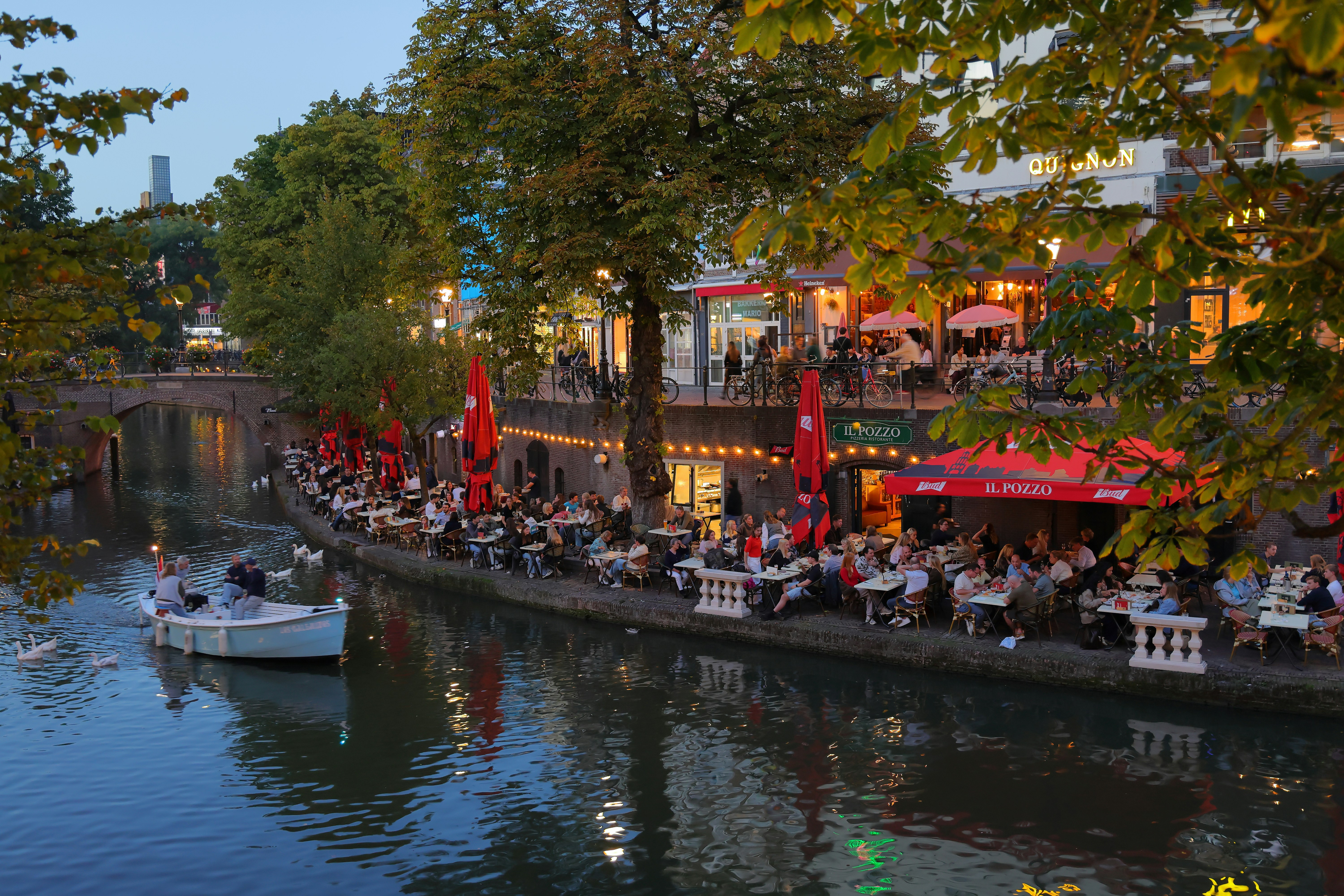 People dining at outdoor tables along a canal in Utrecht with a boat passing
