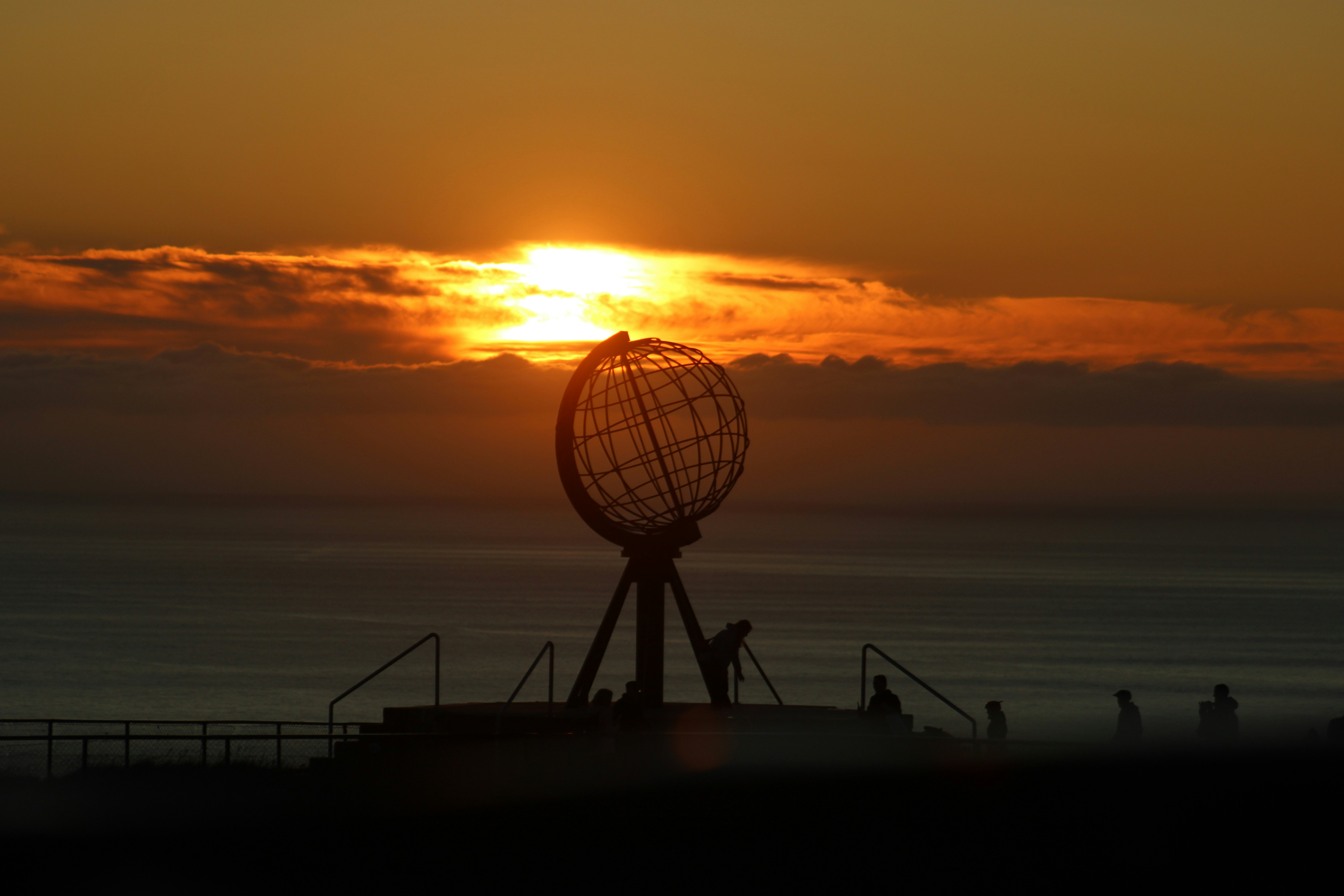 The North Cape globe monument silhouetted against a warm orange sky above the ocean