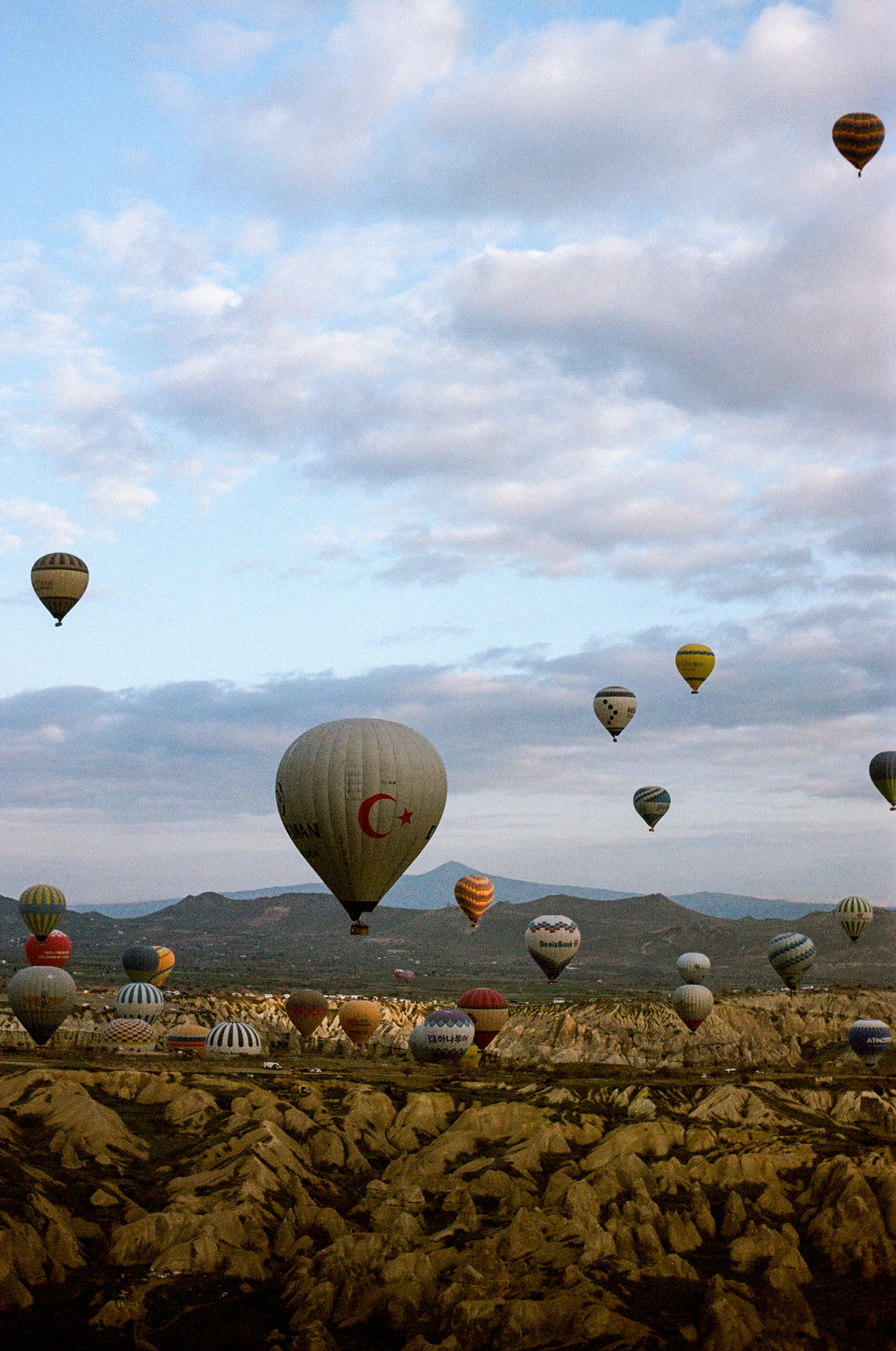 Many hot air balloons floating over the rocky landscape of Cappadocia in Turkey