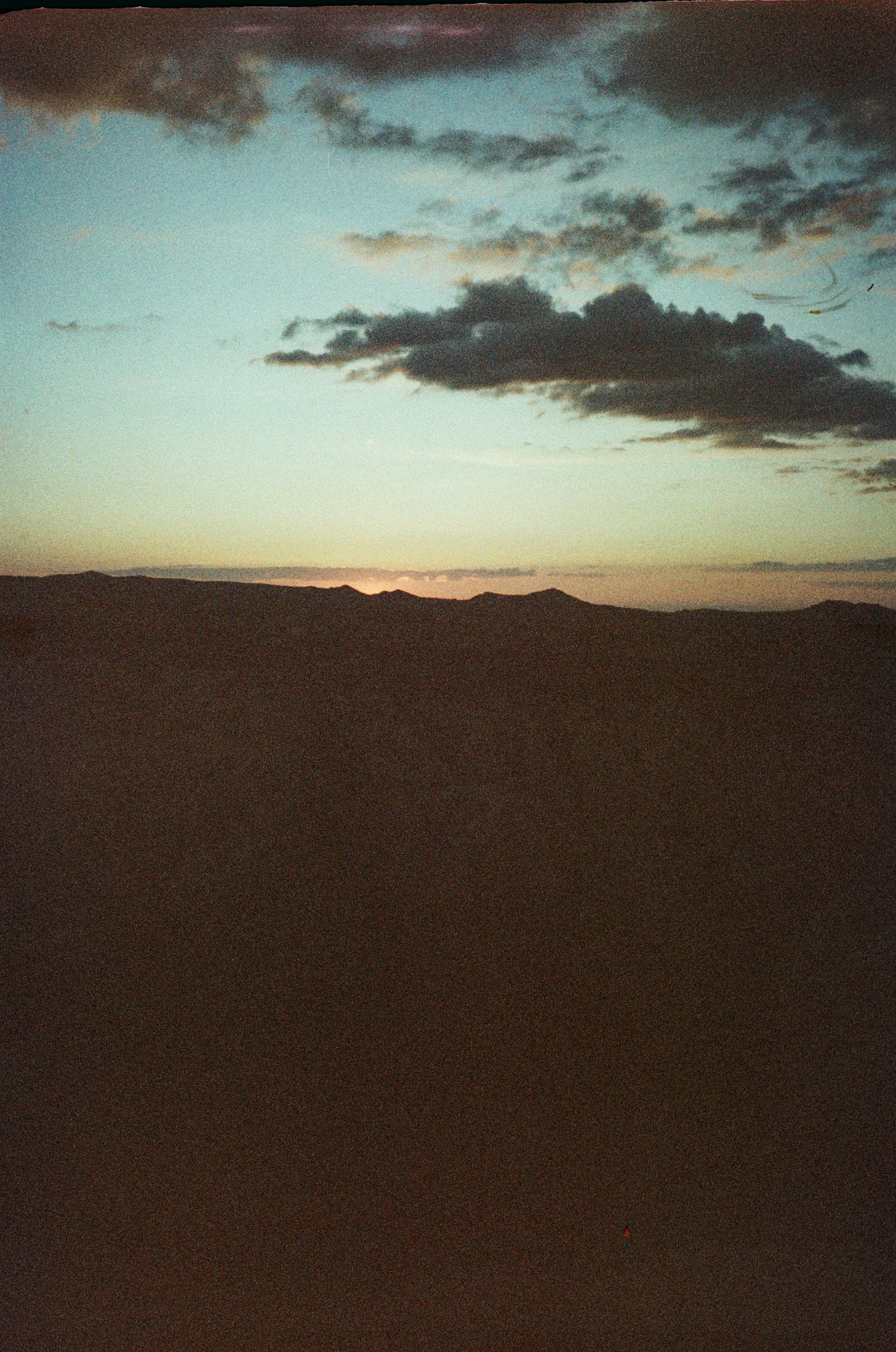 Dark mountain silhouettes against a pale blue sky with scattered clouds