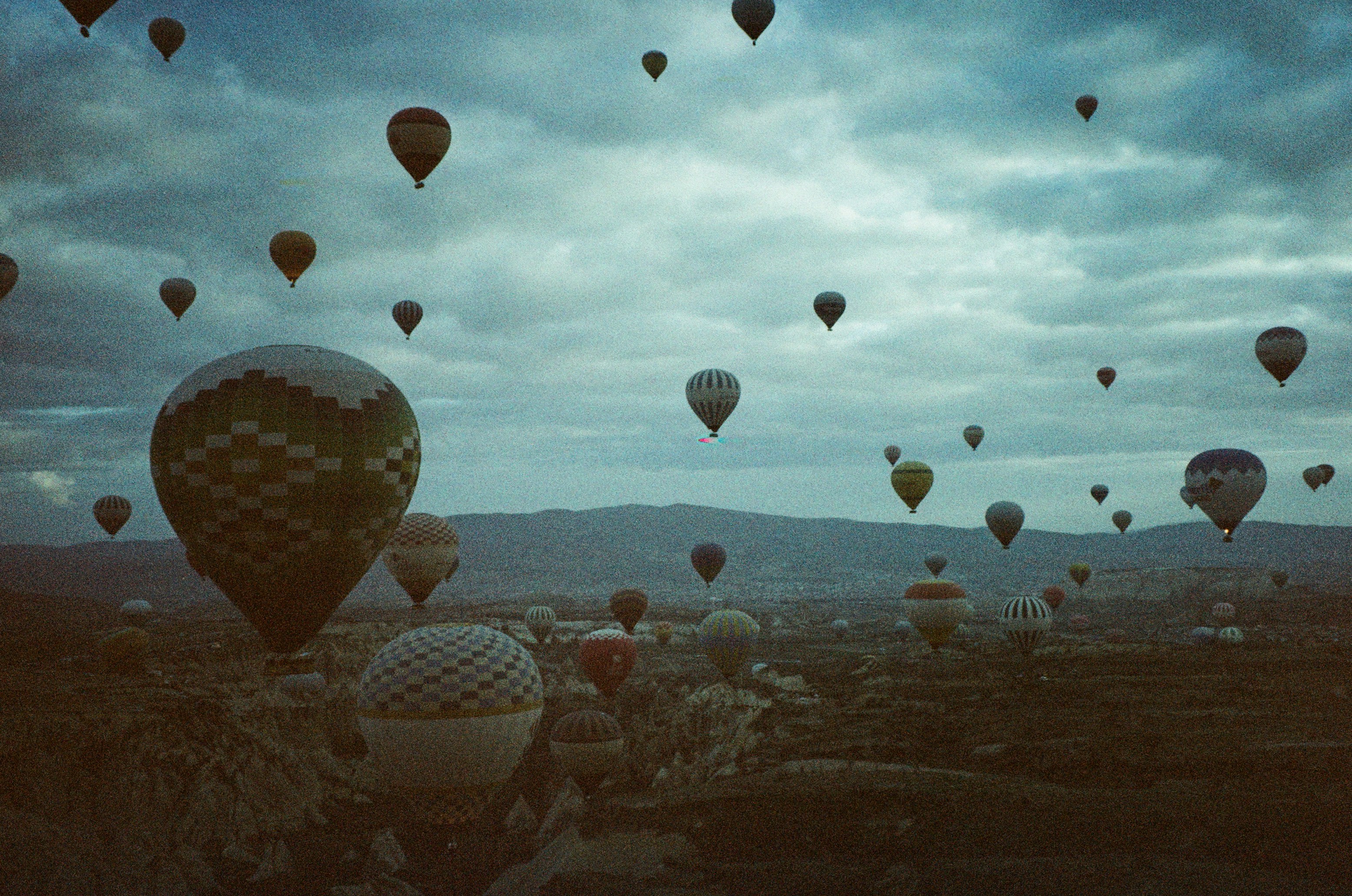 Many hot air balloons floating over a rocky landscape under a cloudy sky