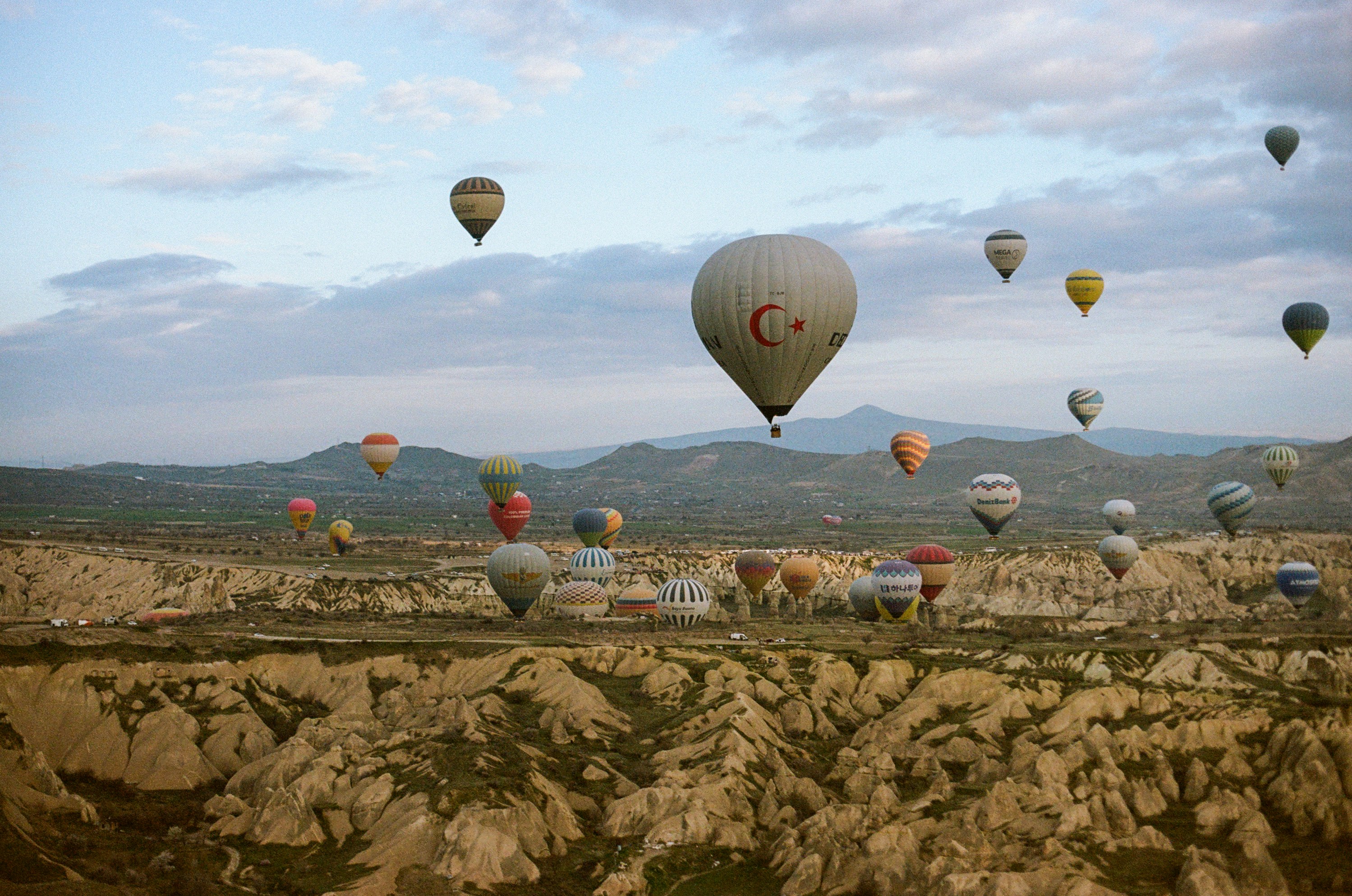 Many colorful hot air balloons floating over the rocky landscape of Cappadocia, Turkey