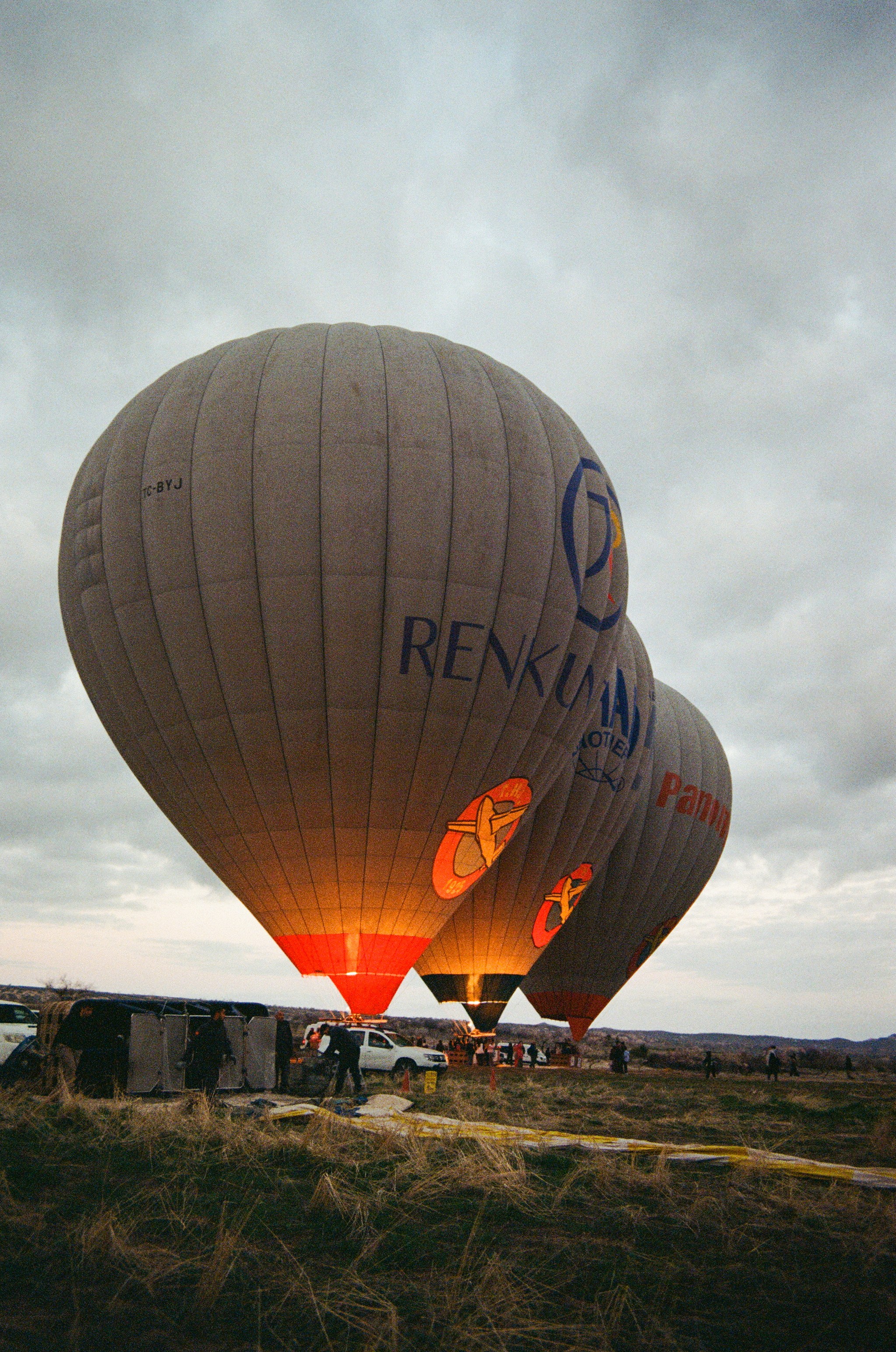 Three hot air balloons with glowing burners on a grassy field under cloudy skies
