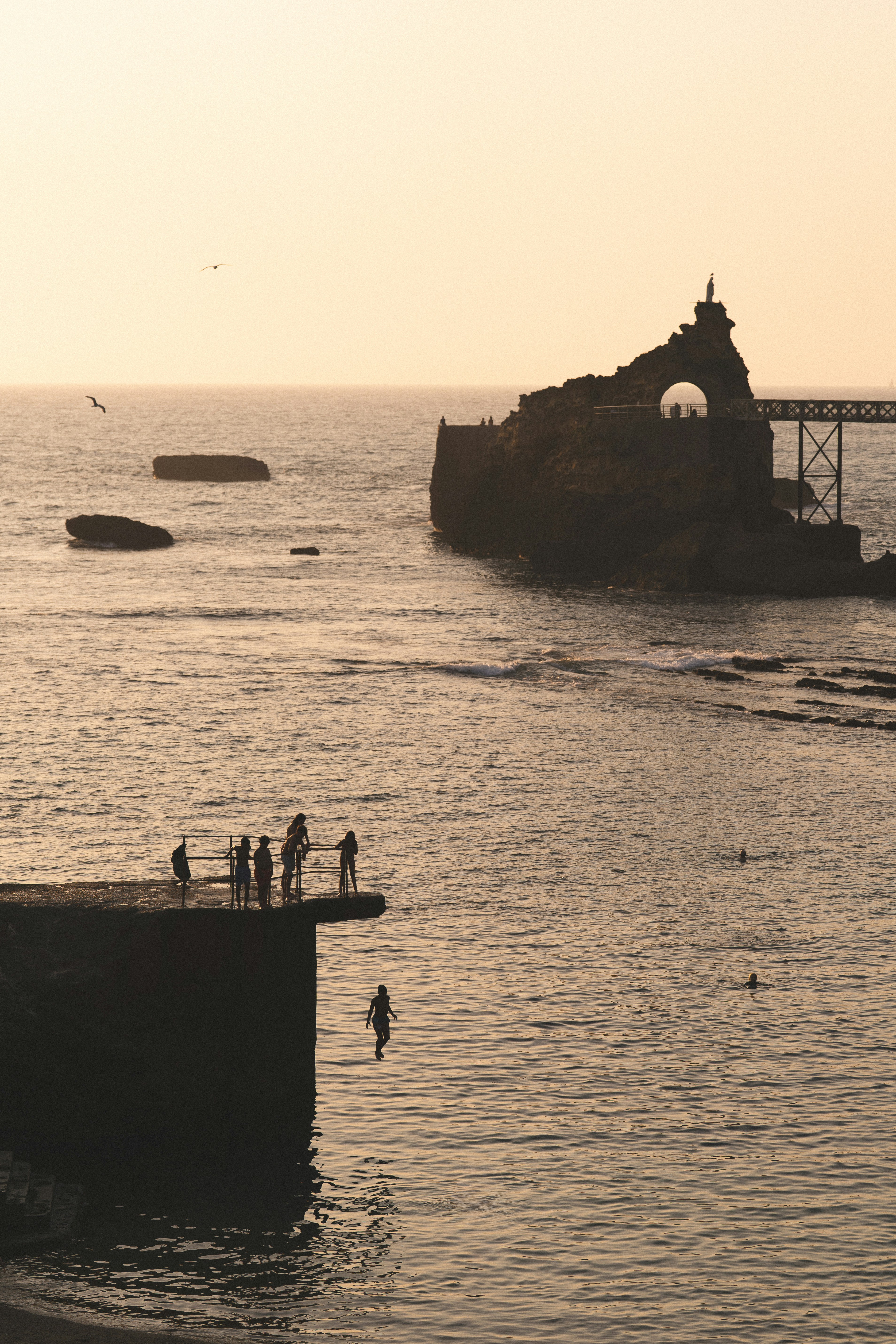 A person jumping from a concrete pier into the ocean at golden hour