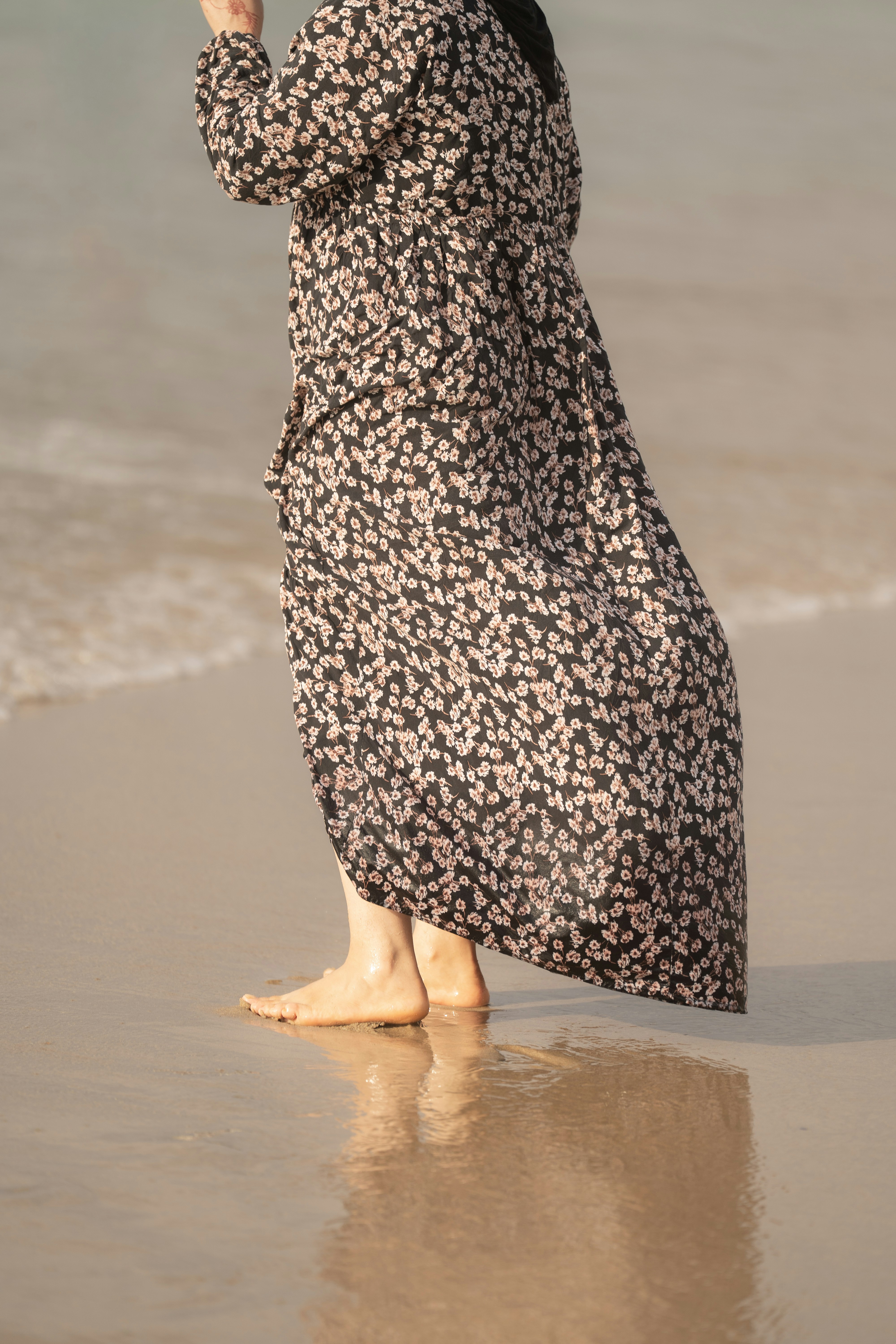 A person in a long floral dress walking barefoot on a sandy beach