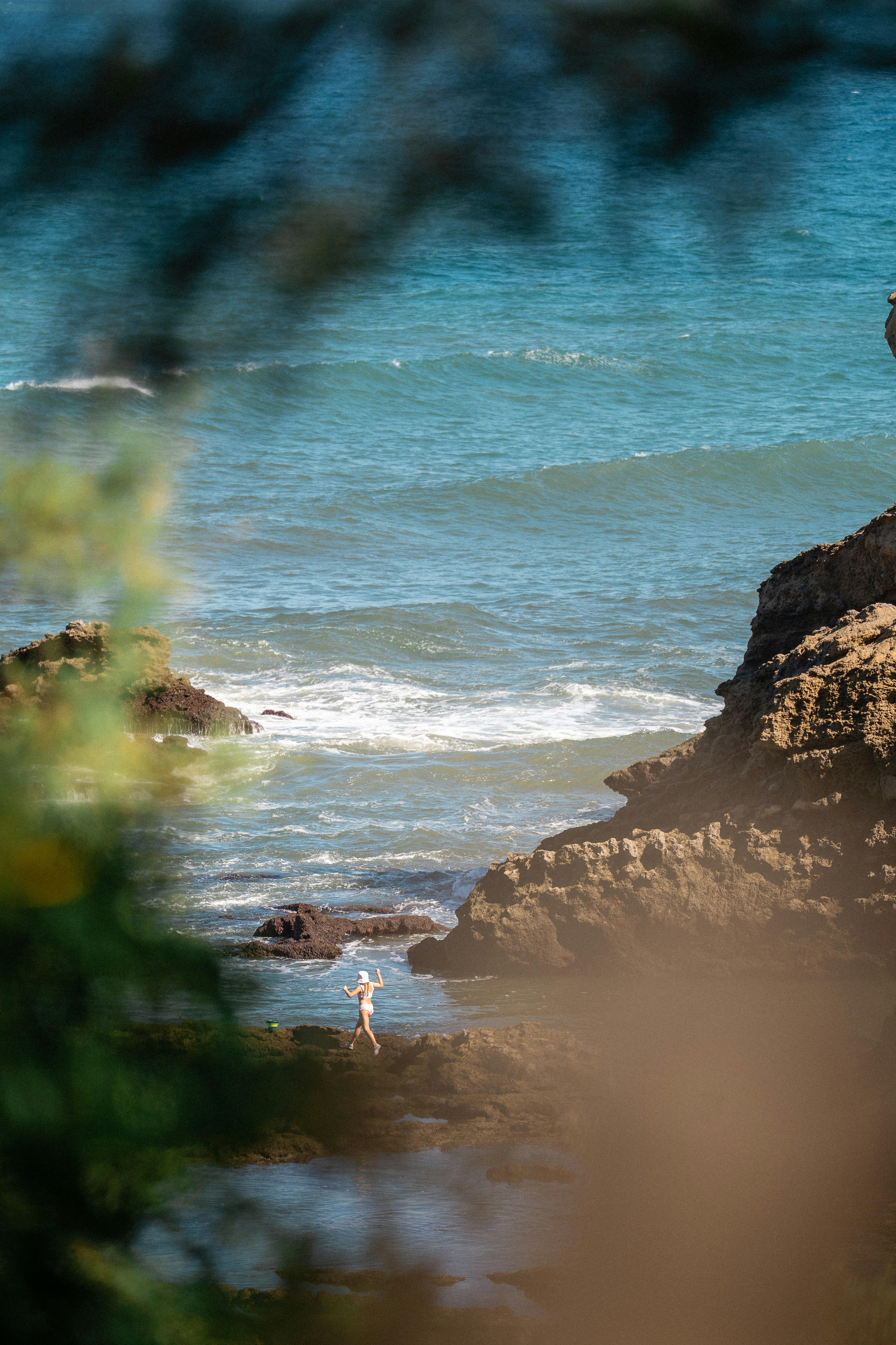 A person in a white bikini and hat walking on rocky coastal tide pools