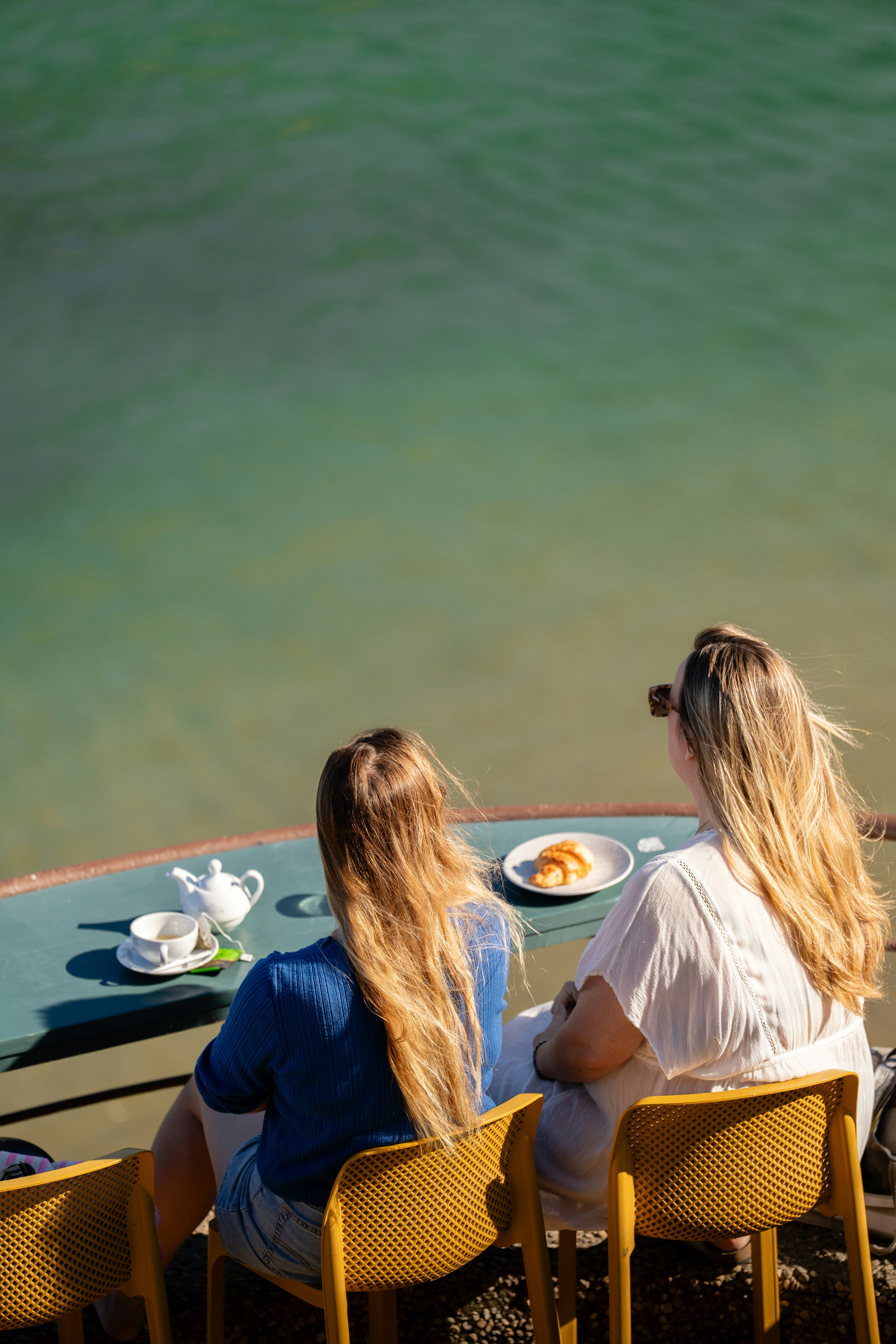 Two women sharing breakfast on a sunny terrace by the ocean