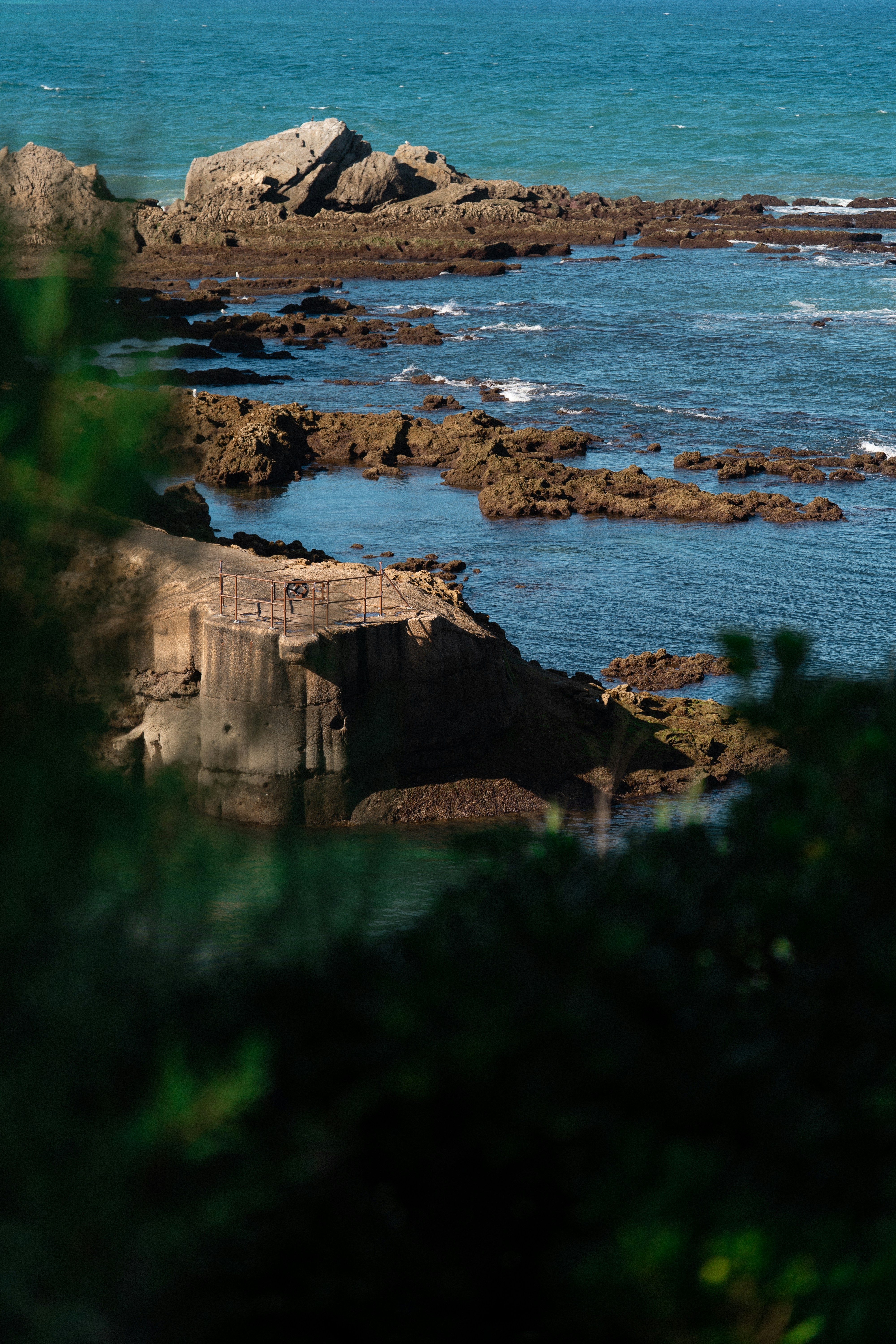 A concrete platform with a metal railing on a rocky coastline by the ocean
