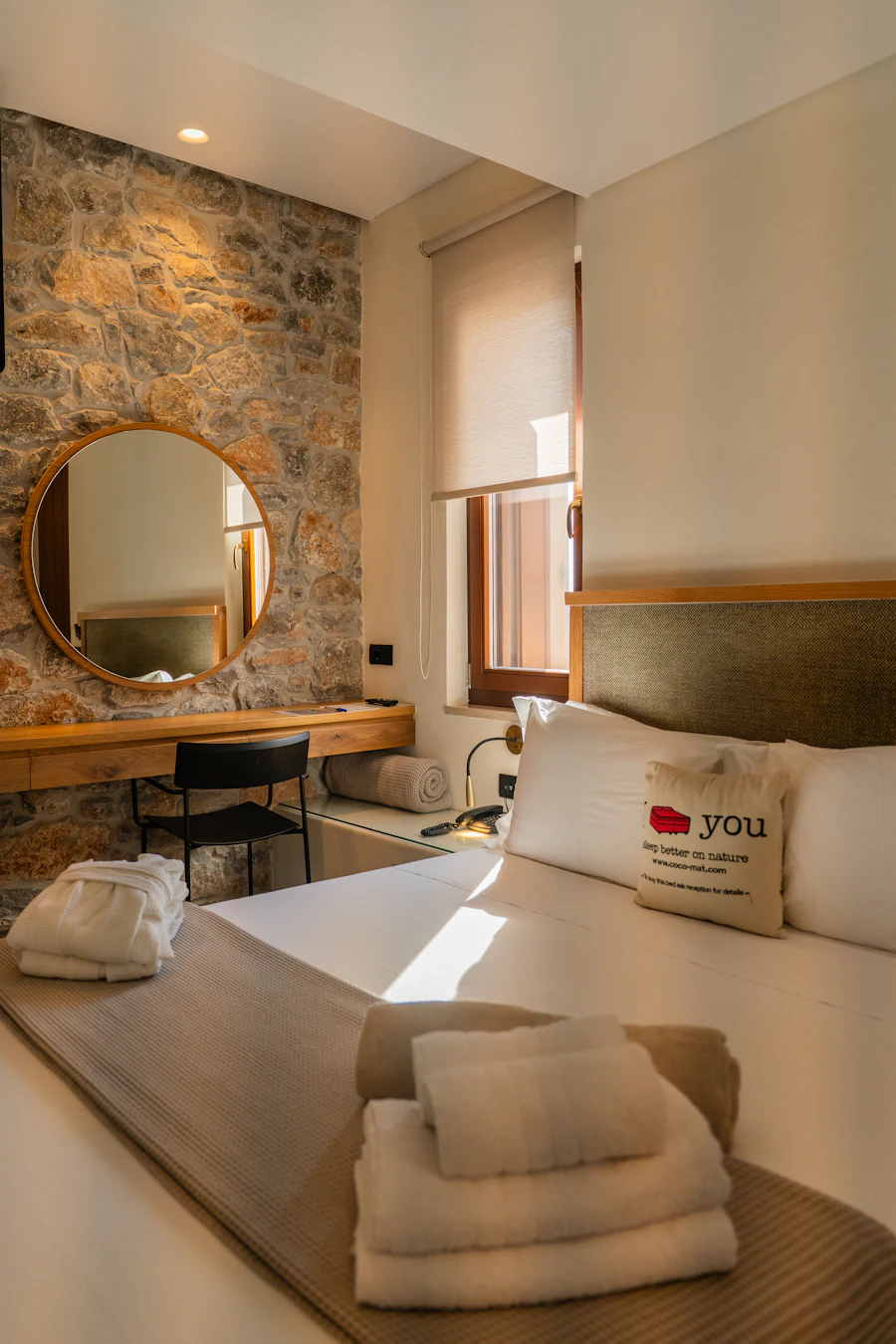 Bedroom with stone wall, round mirror and white linens