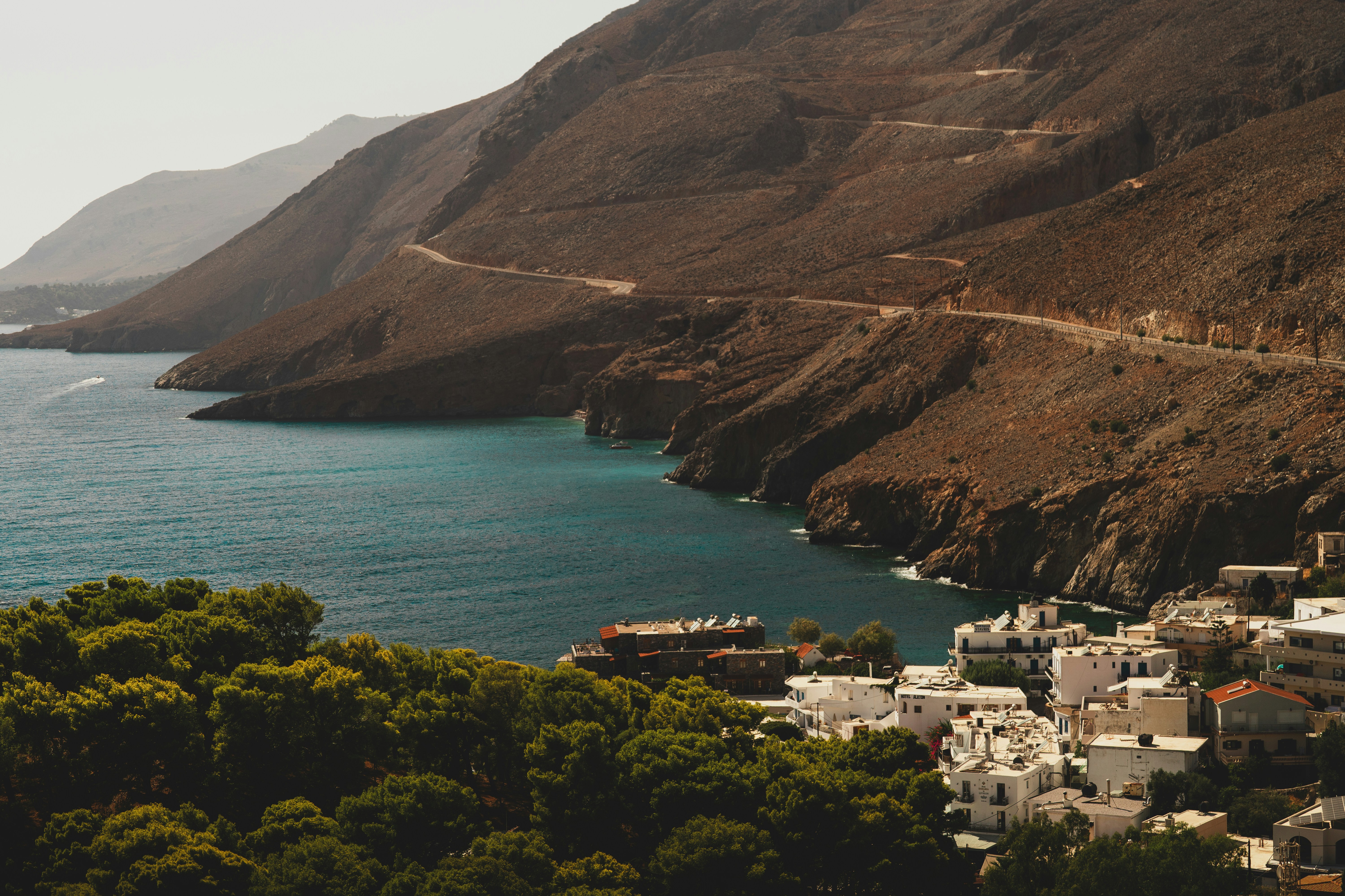 A coastal village with white buildings nestled below a winding road on rocky cliffs
