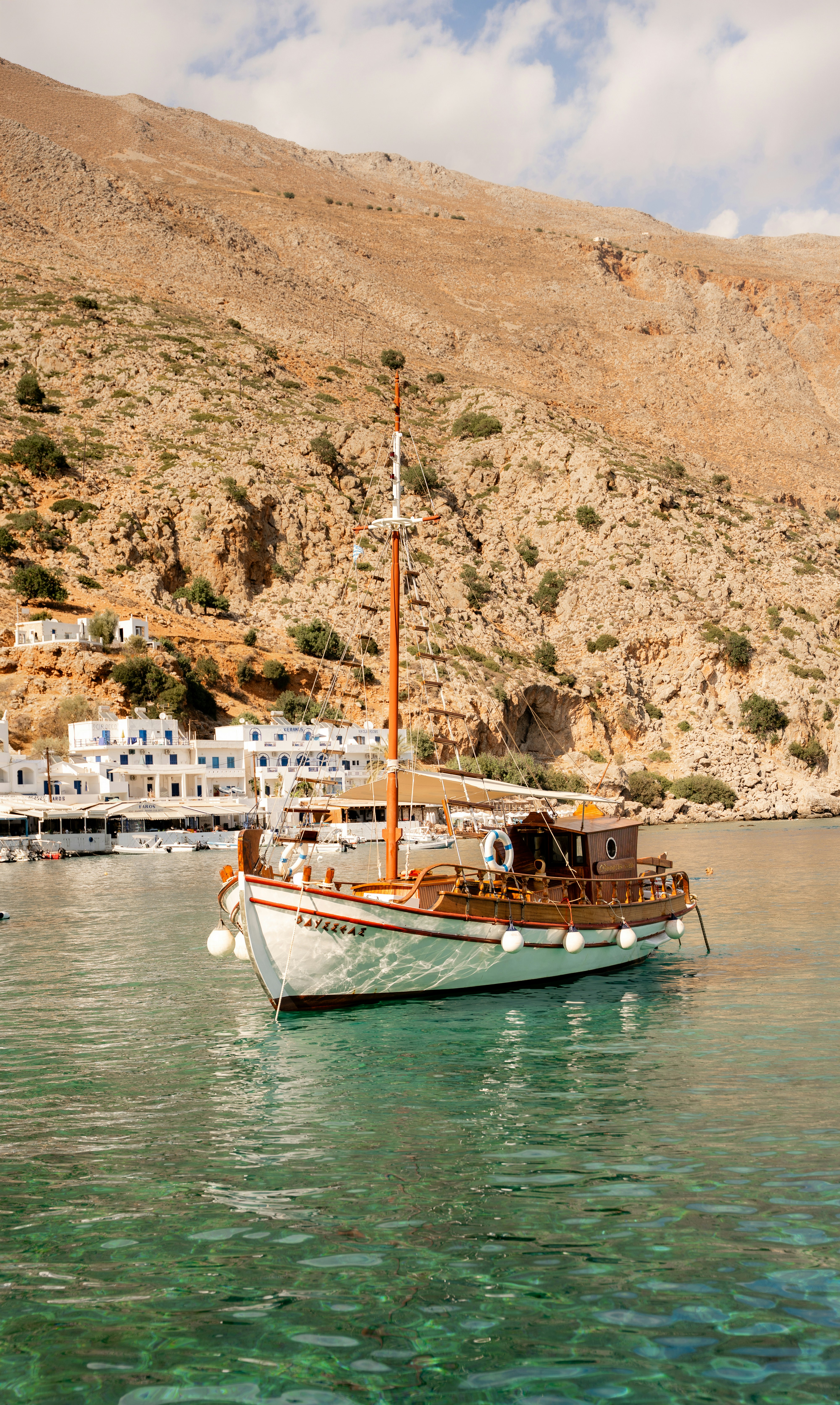 A wooden fishing boat anchored in clear water in front of a white village