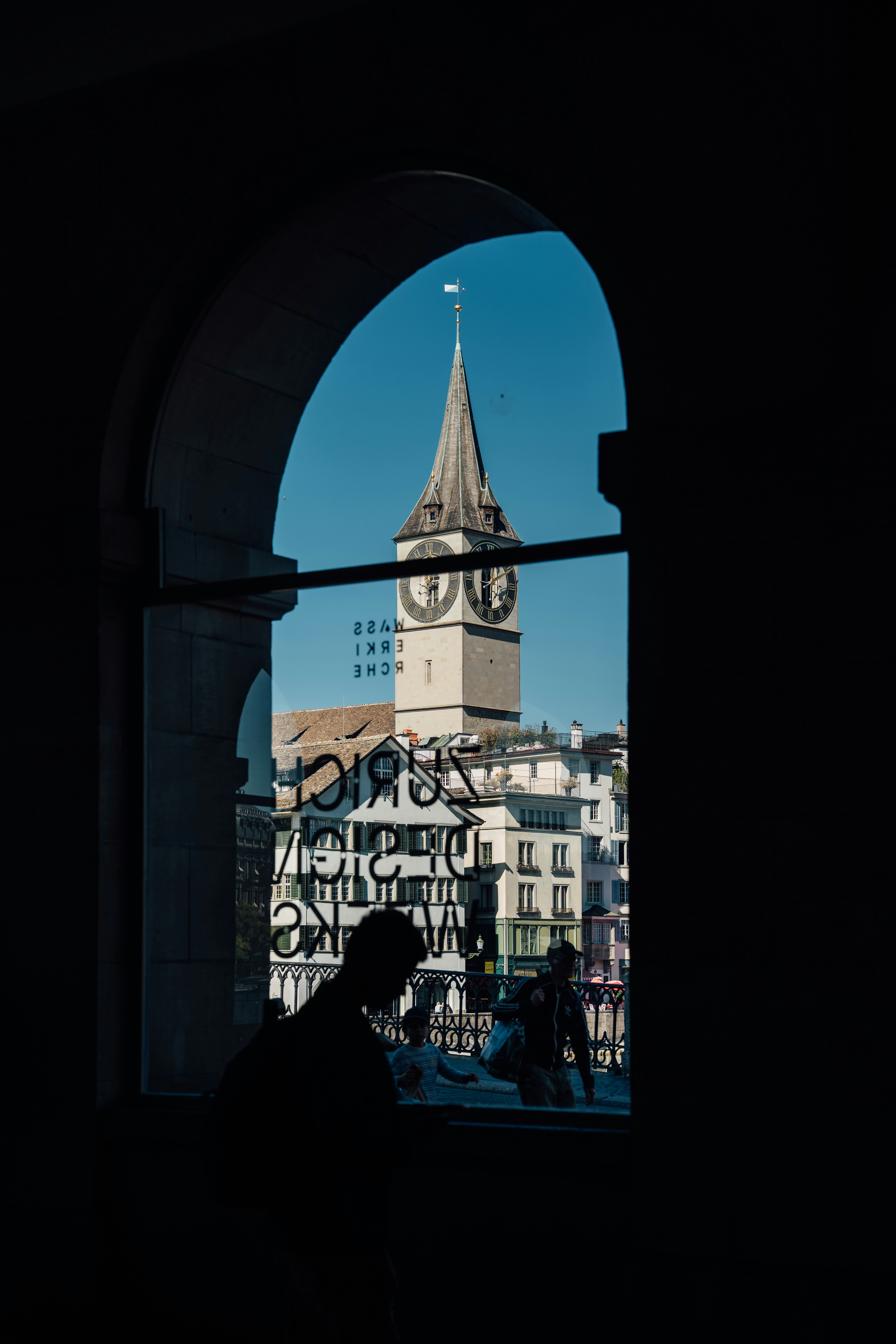 La tour de l’église Saint-Pierre vue à travers une fenêtre avec des silhouettes de personnes à Zurich