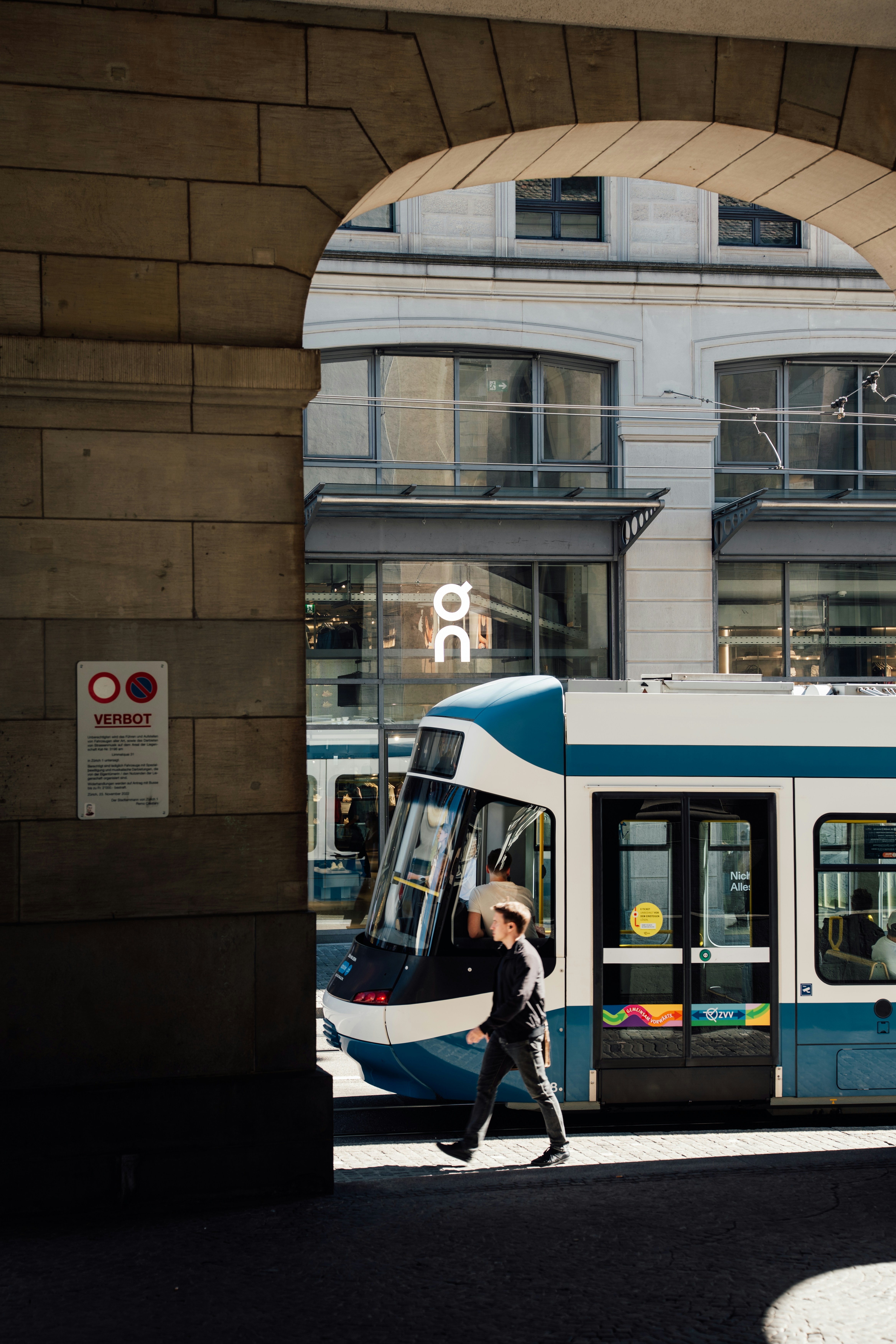 Une personne passant devant un tramway bleu et blanc dans une rue de la ville