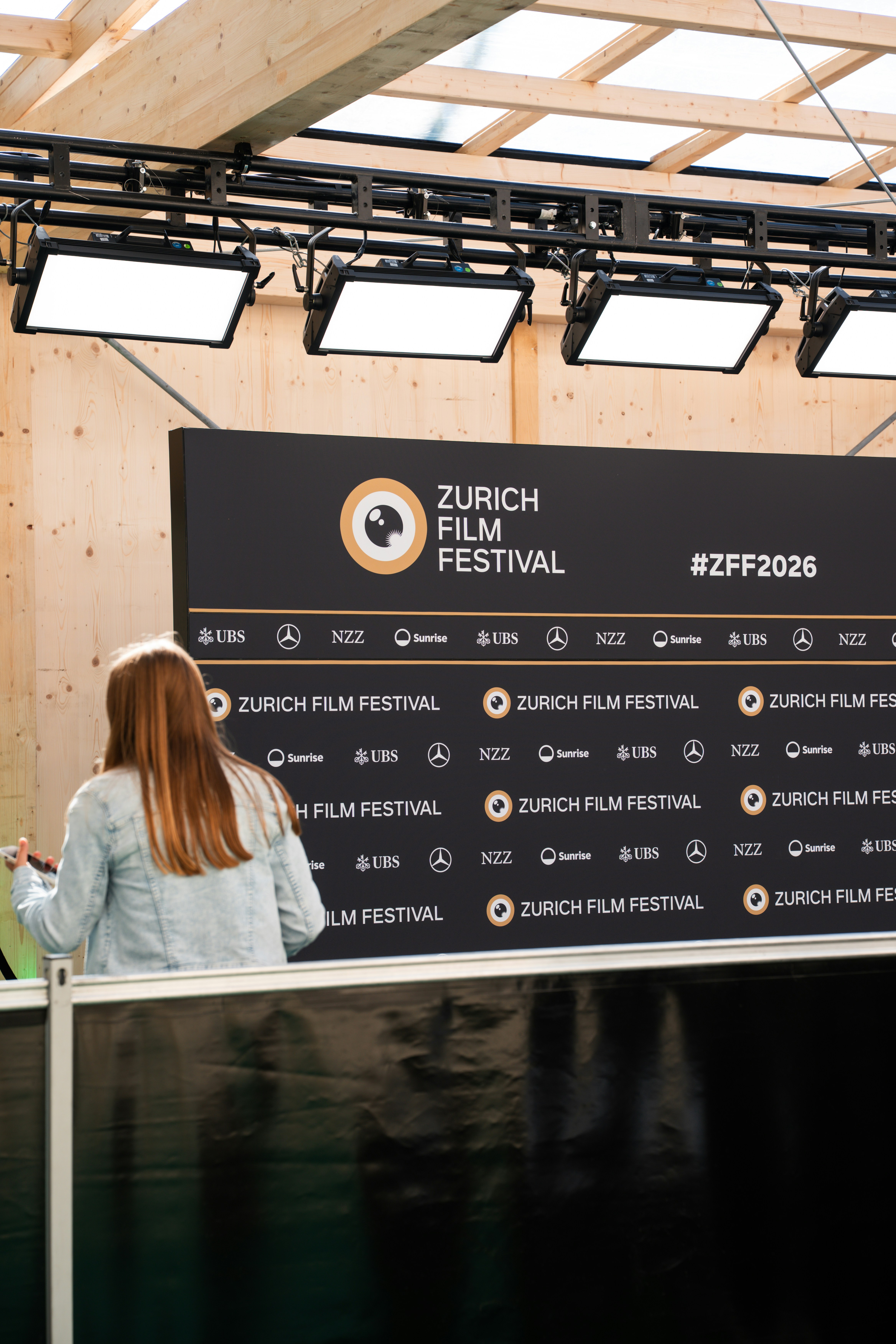 Une personne en veste en jean debout devant un décor du Festival du film de Zurich