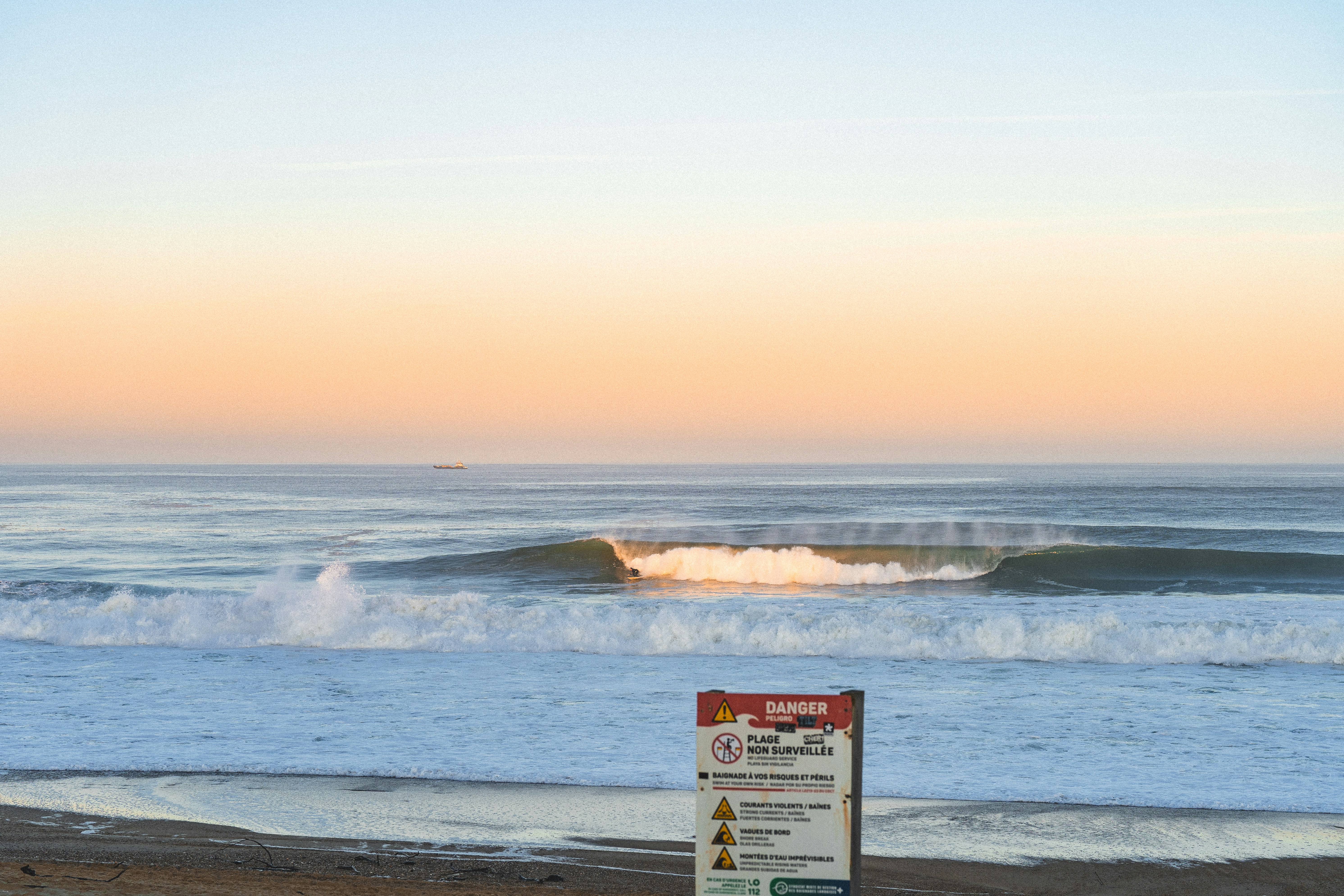 A surfer riding a breaking wave at the beach with a danger sign
