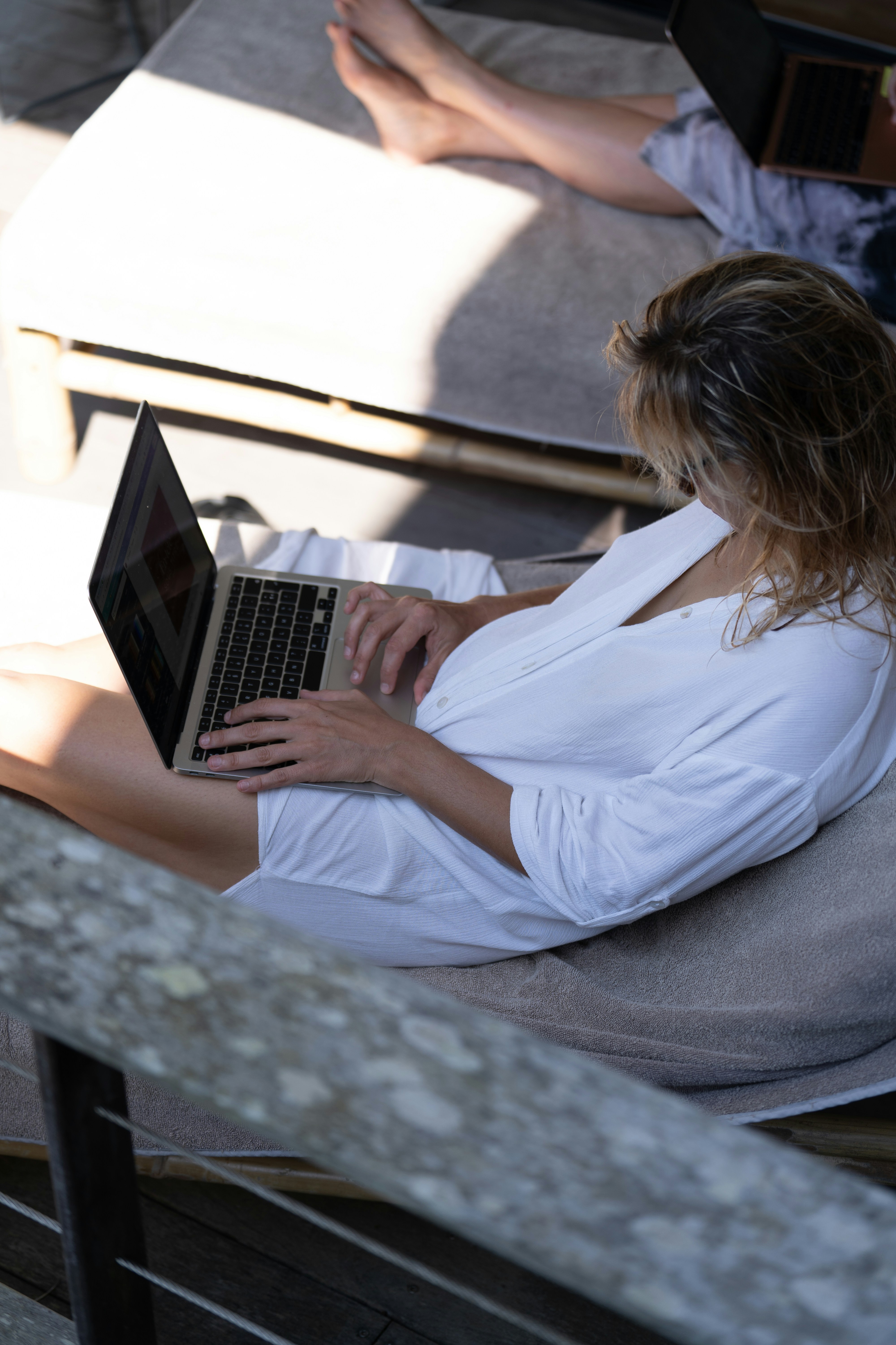 Une femme en chemise blanche tapant sur un ordinateur portable sur une chaise longue