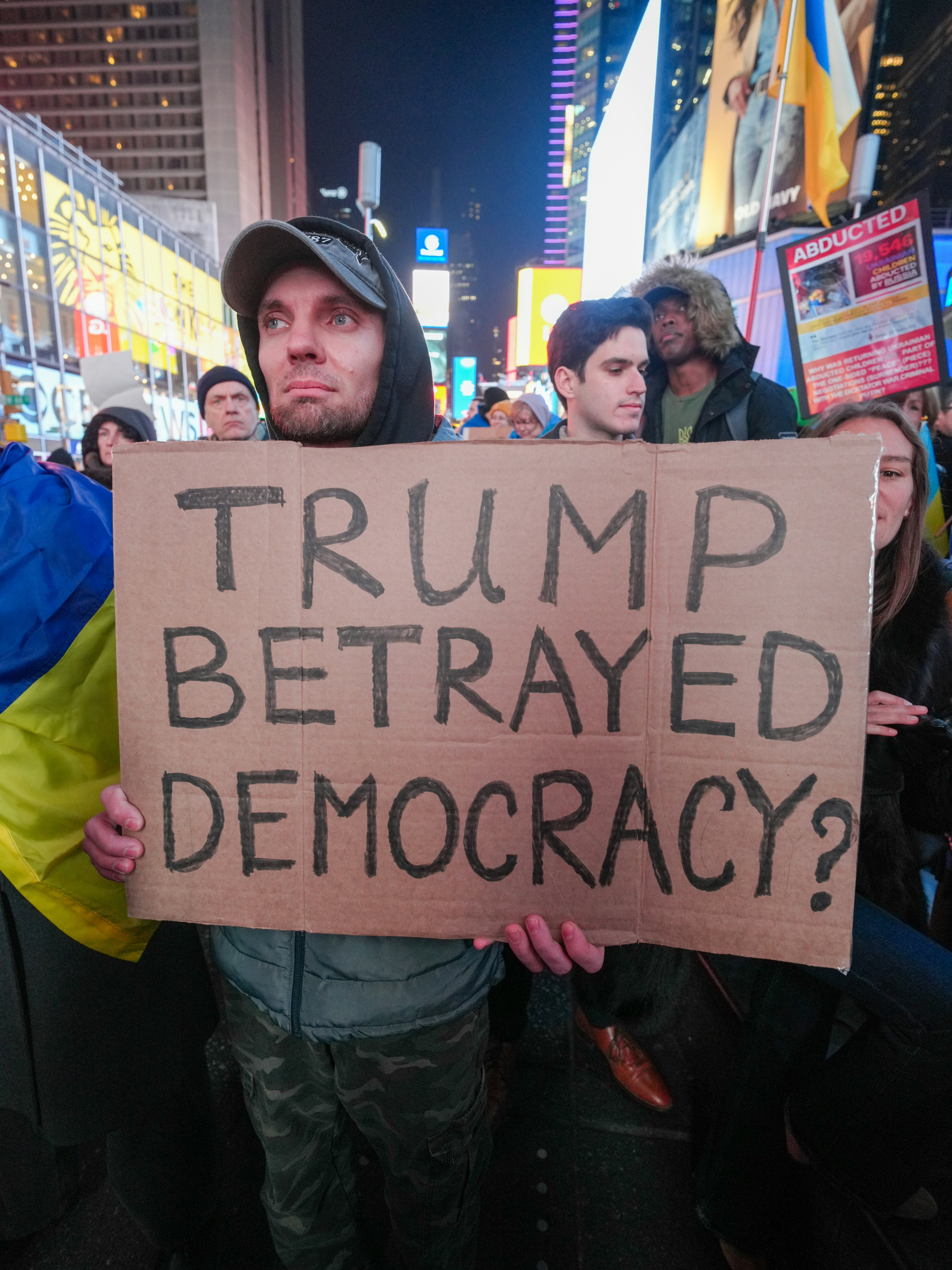 Un uomo che tiene un cartello di cartone con scritto TRUMP HA TRADITO LA DEMOCRAZIA in una folla cittadina