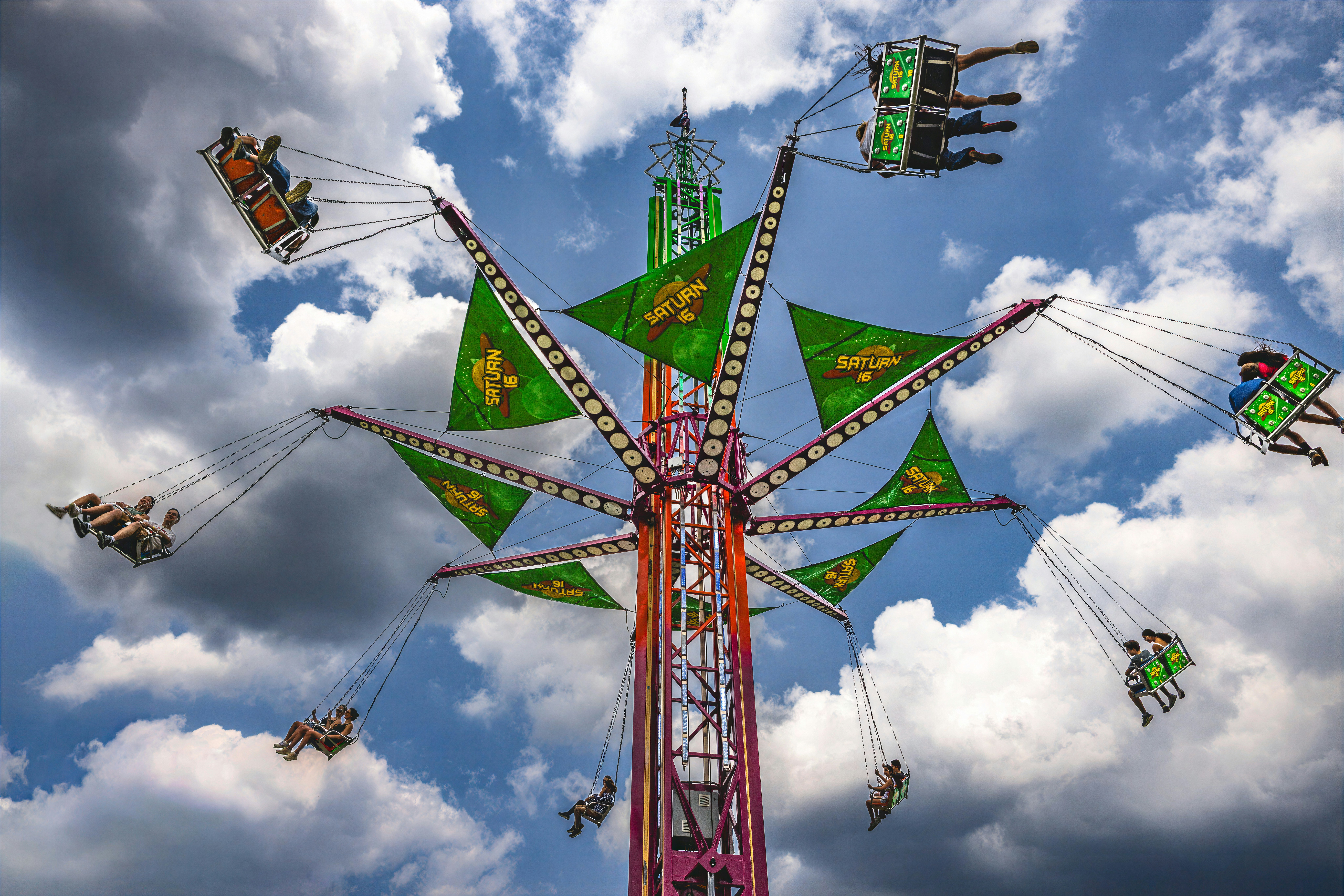 People riding a Saturn 16 swing ride against a blue sky with clouds