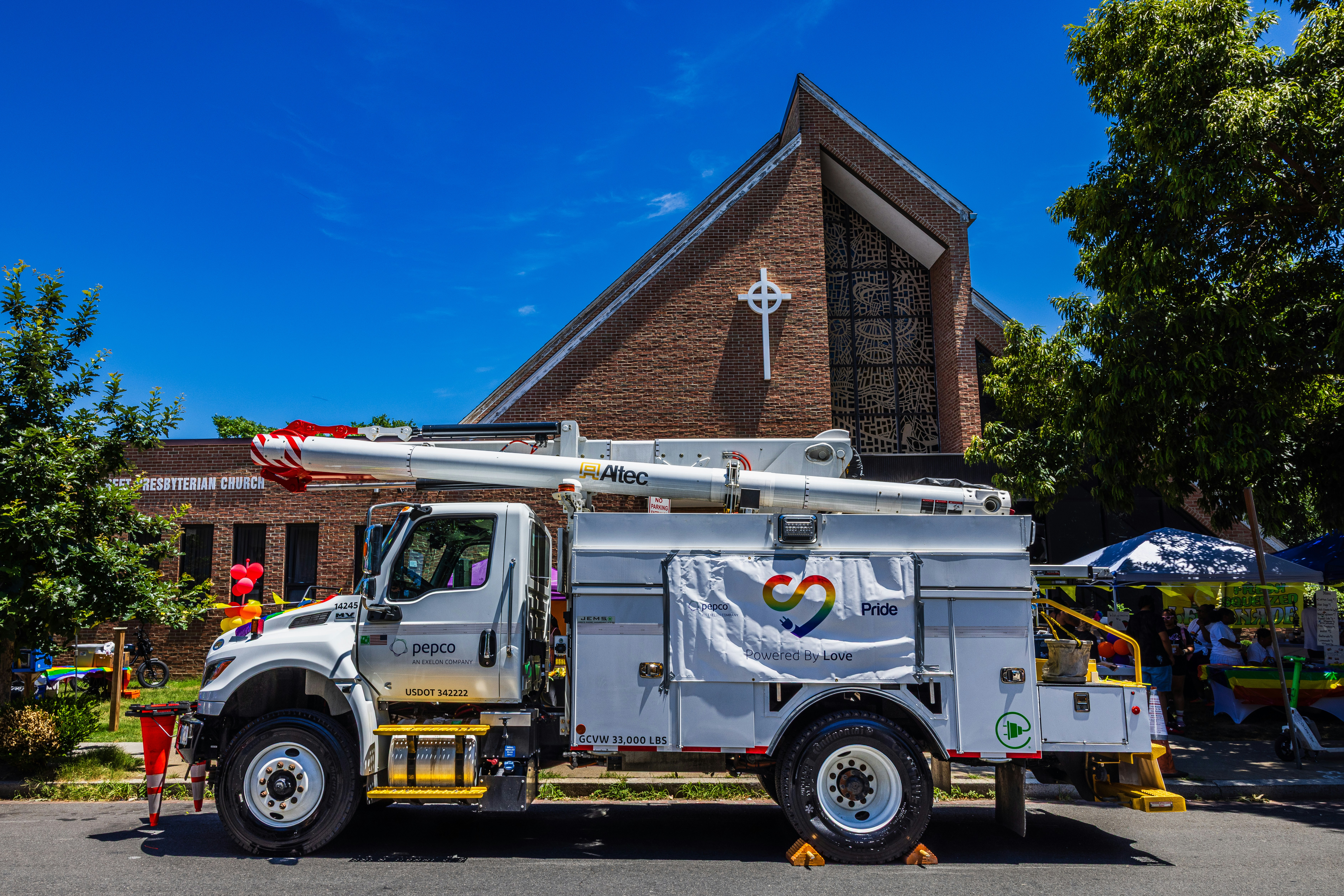 A white utility truck with a rainbow heart logo parked before a brick church