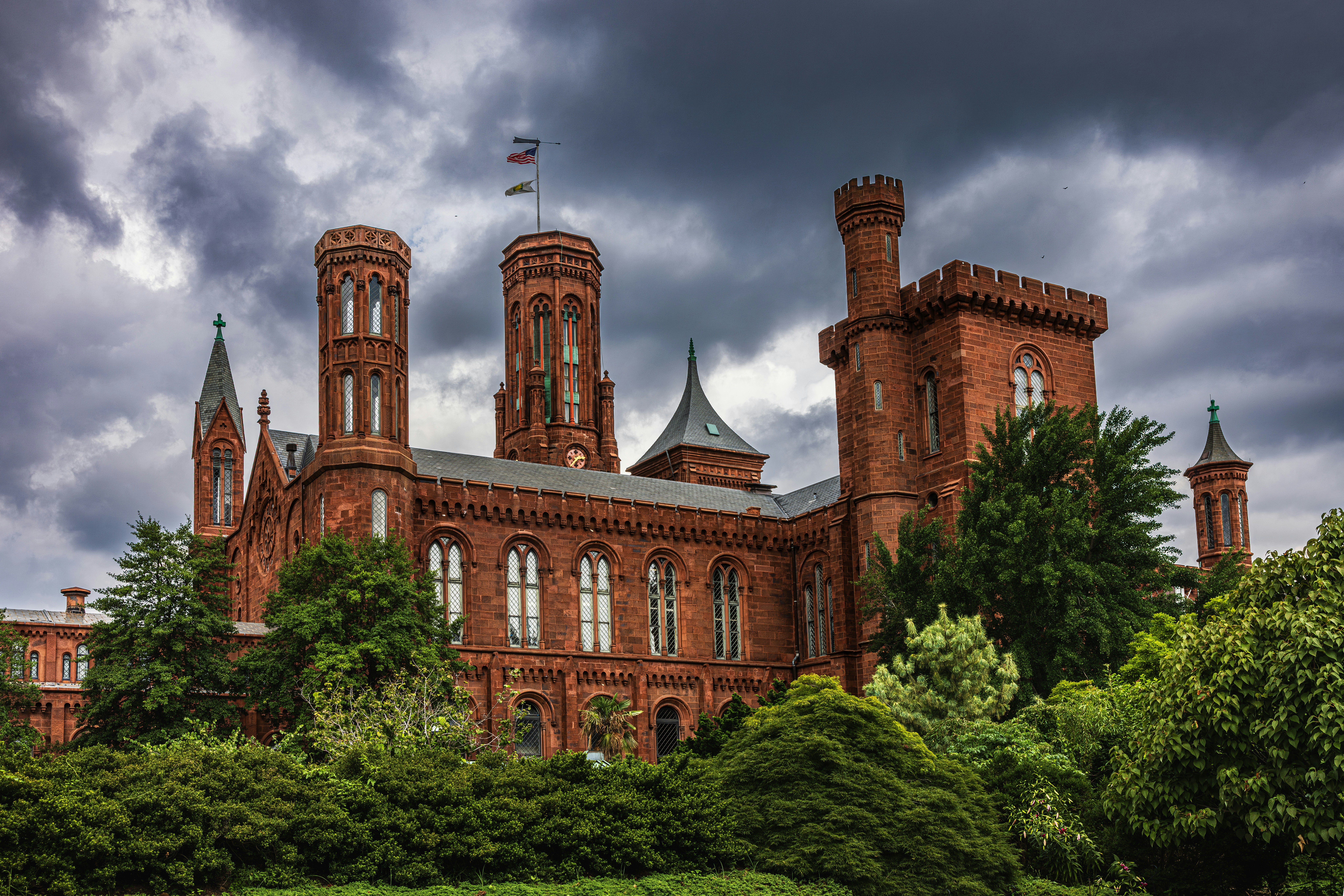 The Smithsonian Institution Building in red sandstone surrounded by lush green trees under storm clouds