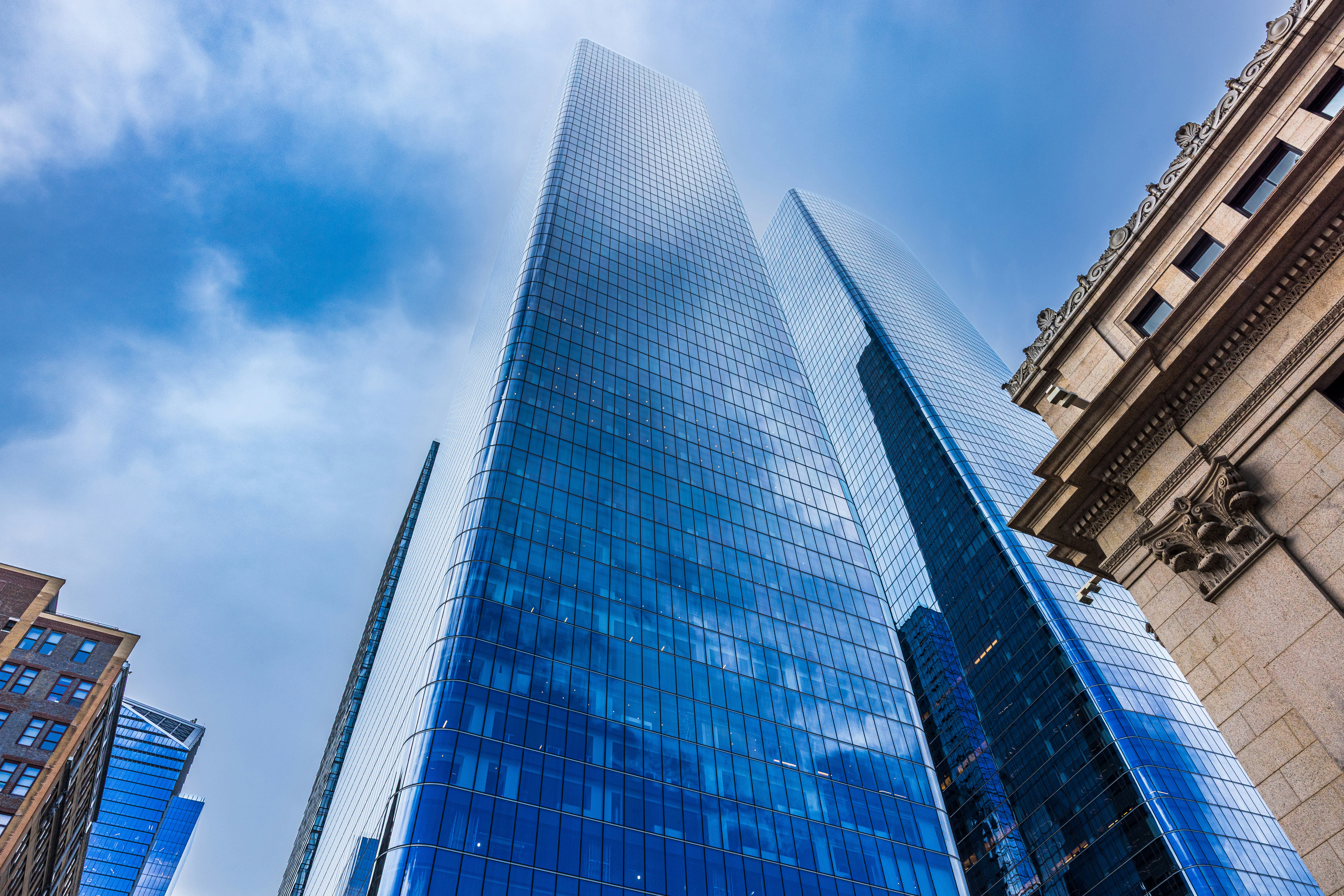 Modern glass skyscrapers rising into a cloudy blue sky beside a stone building