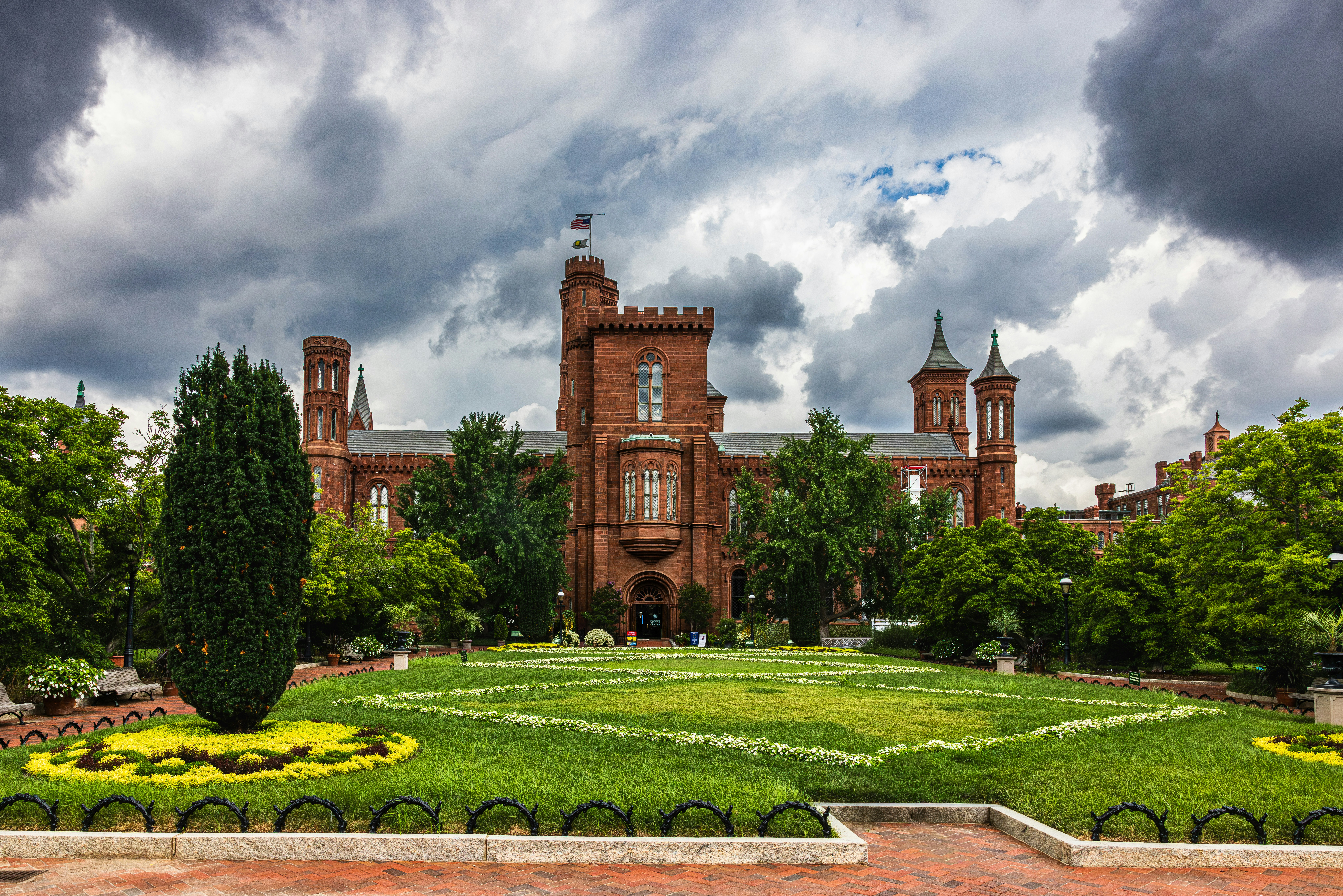 The Smithsonian Institution Building in Washington DC surrounded by green gardens under cloudy skies