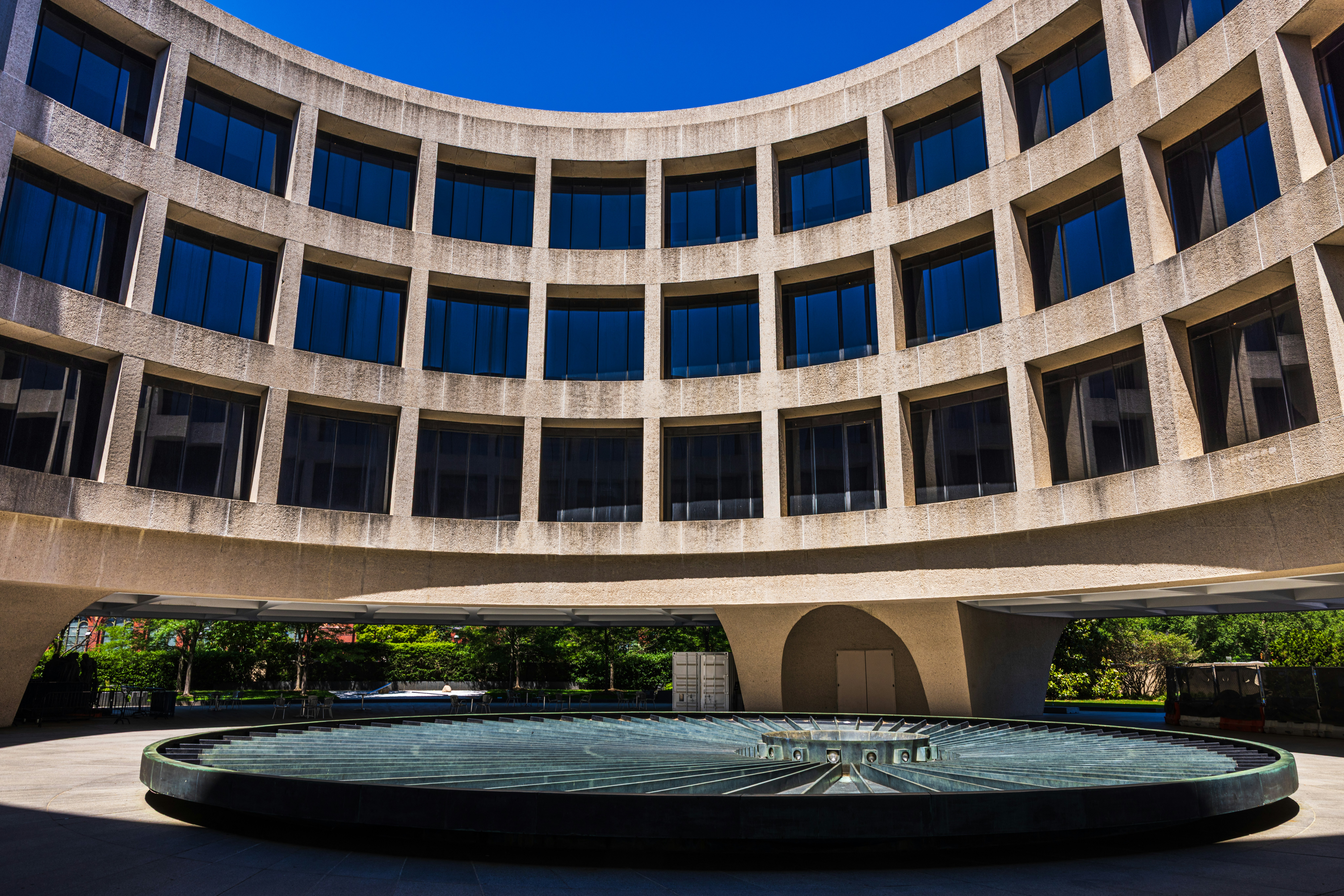 A circular concrete building with dark windows surrounding a large metal fountain