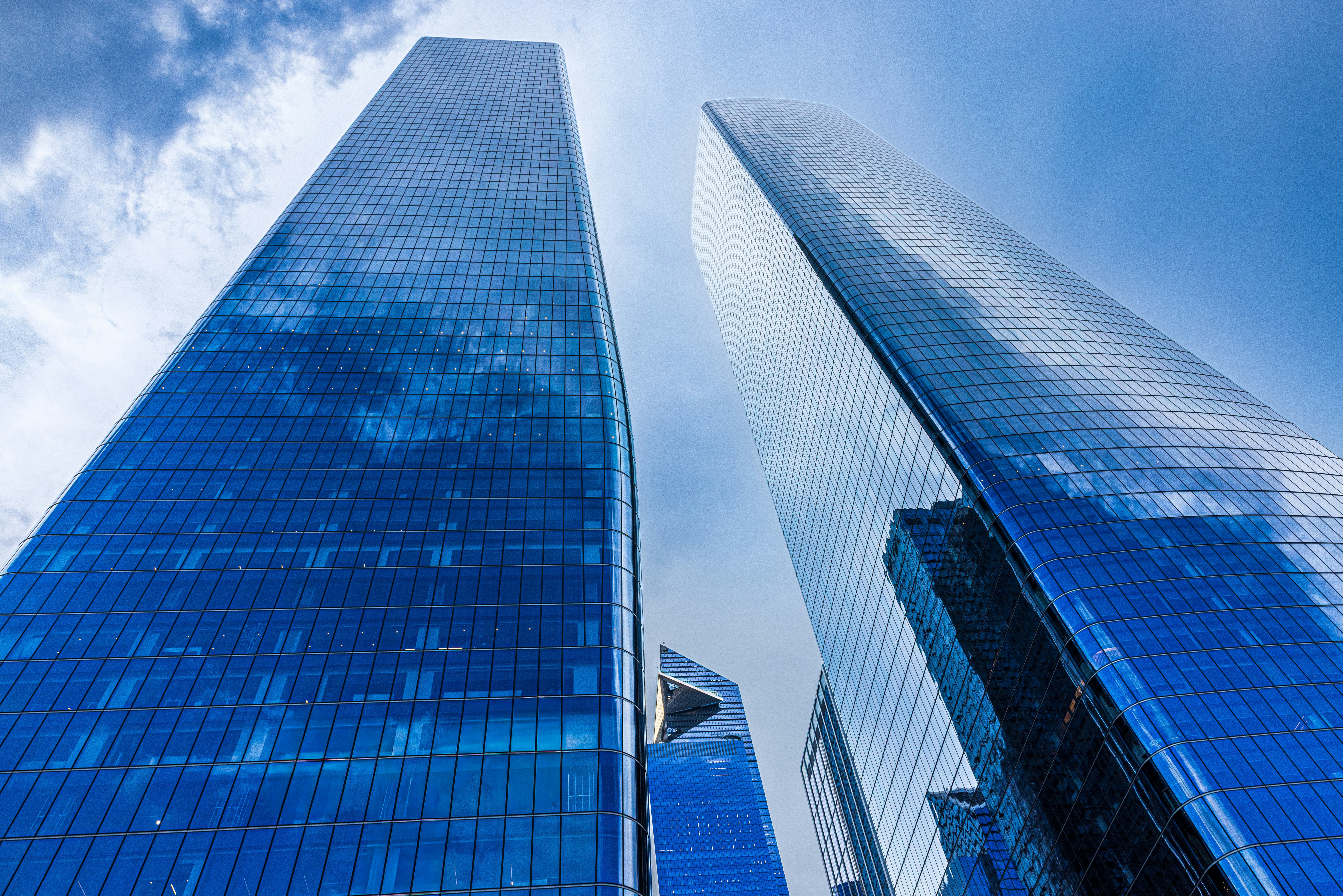 Two tall glass skyscrapers reflecting a blue sky with clouds from below