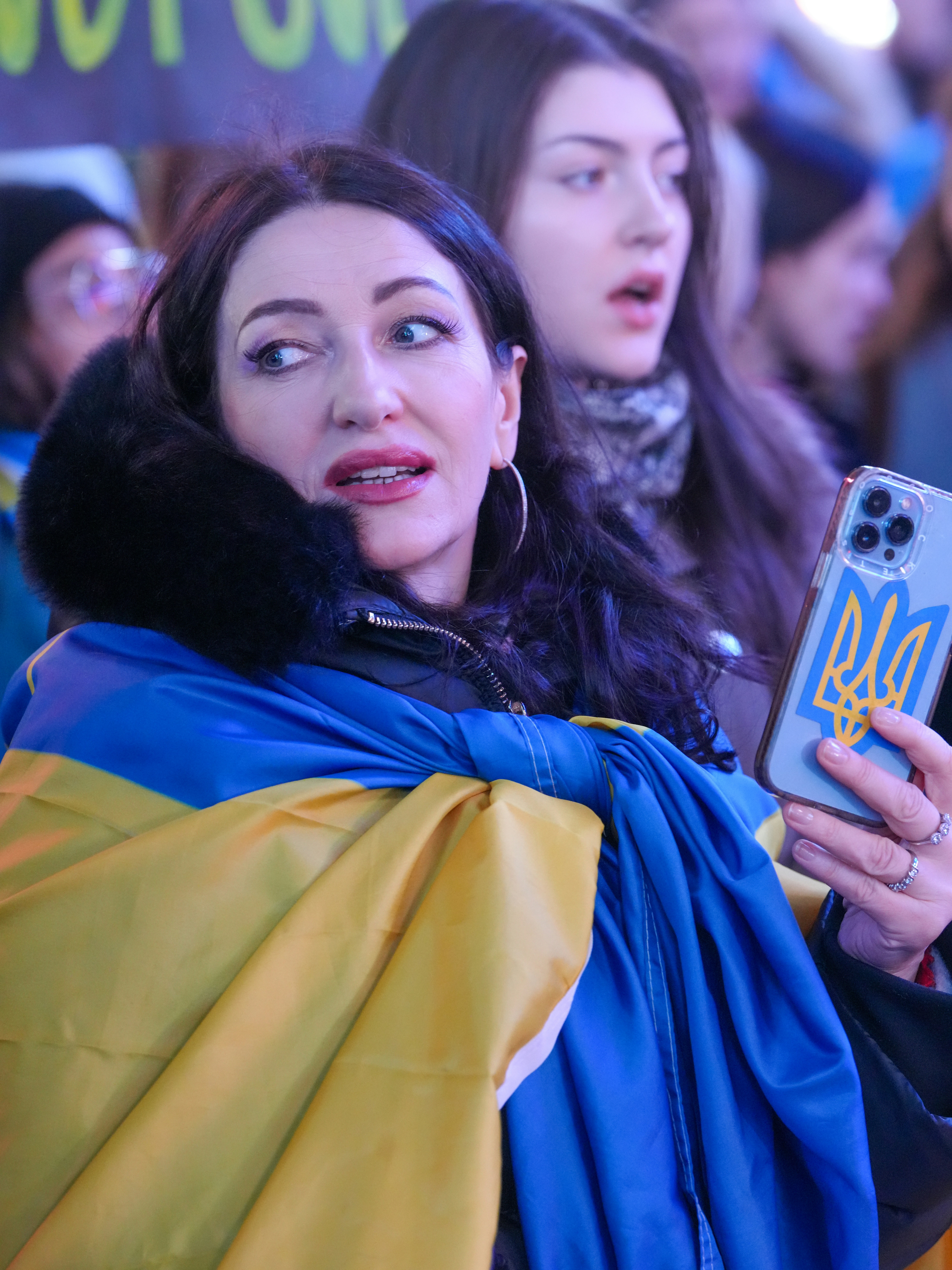 A woman wrapped in a blue and yellow flag holding a smartphone