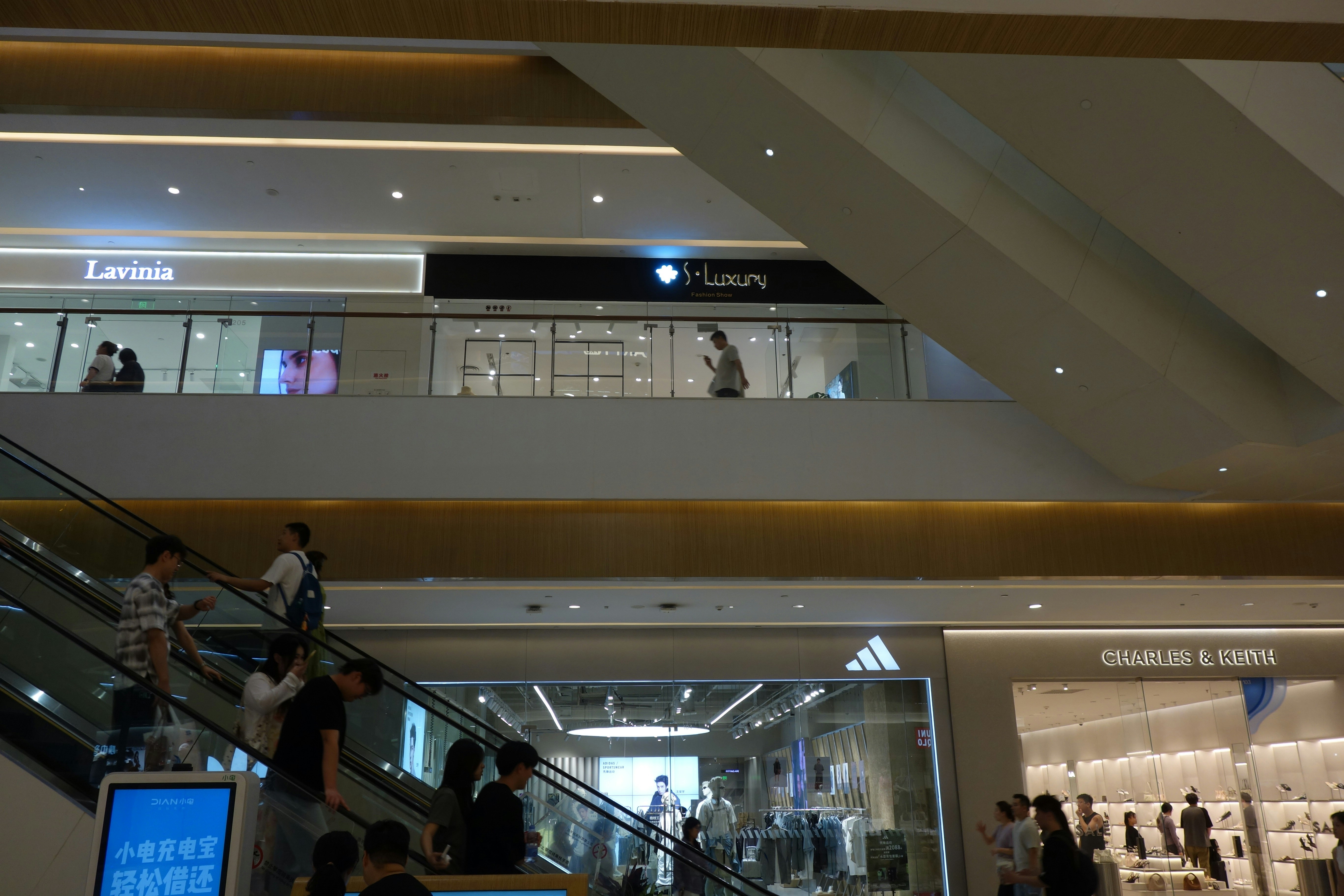 People on an escalator in a multi-level shopping mall with retail storefronts