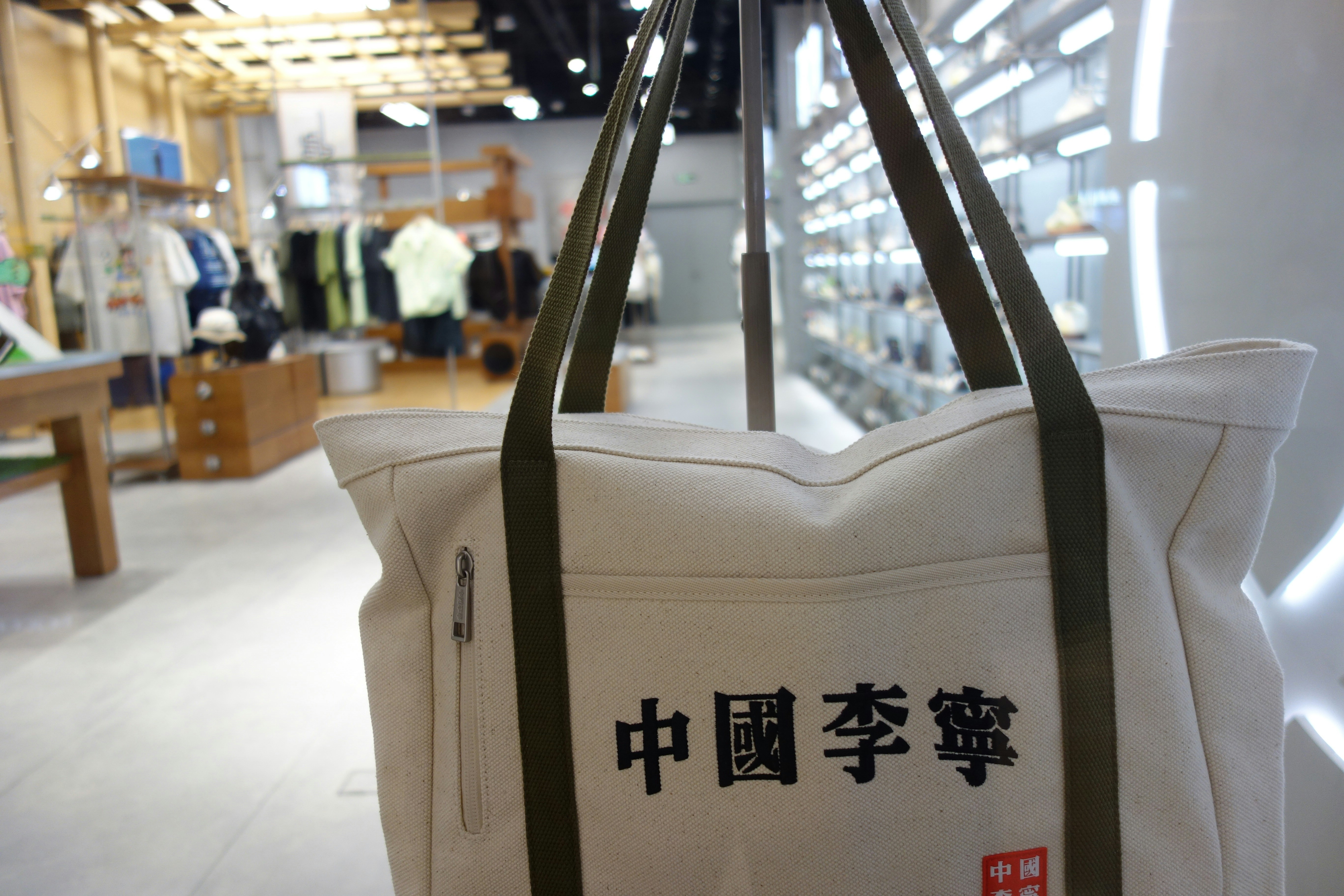 A canvas tote bag with green straps in a retail clothing store