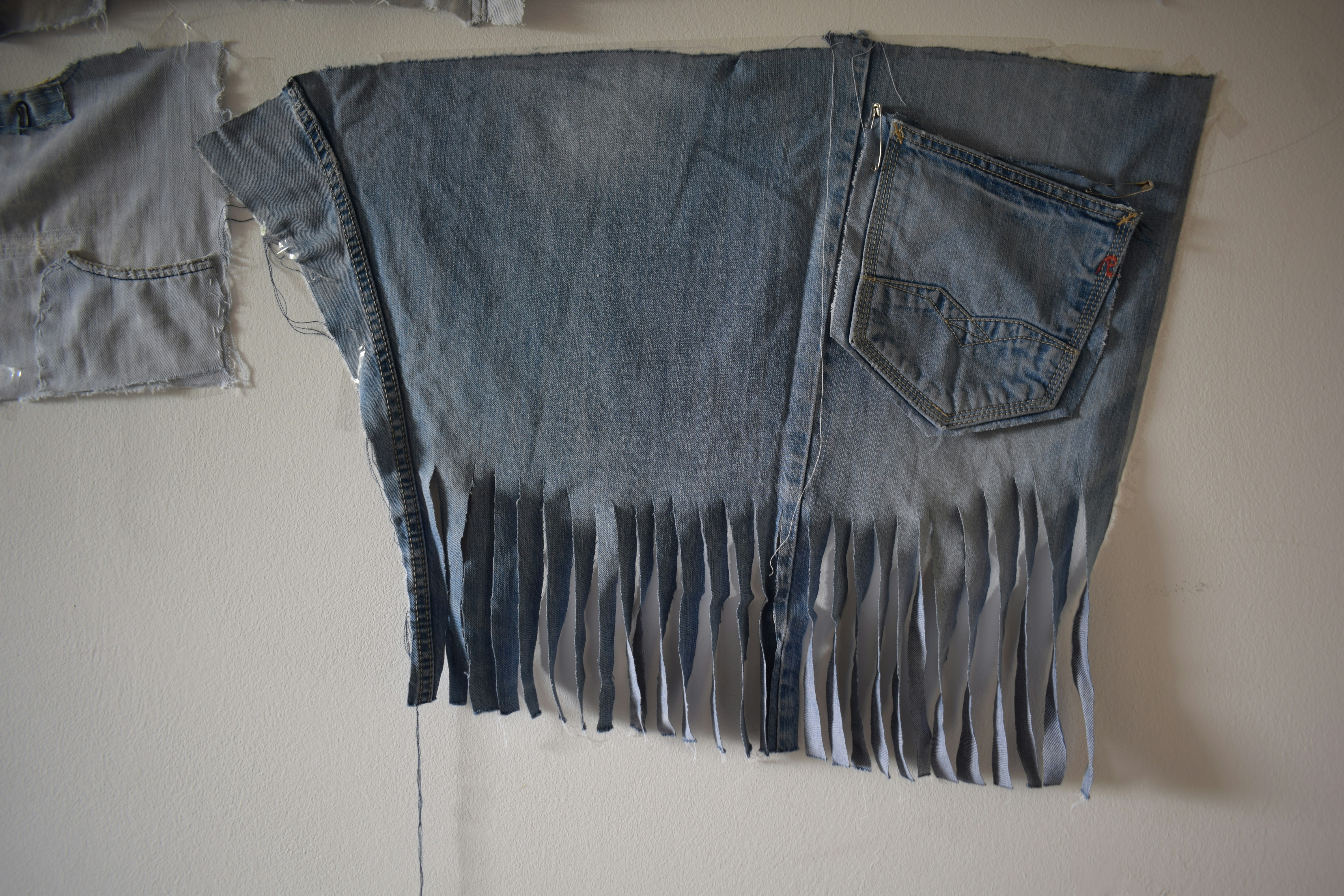 A piece of blue denim fabric with fringe cut into the bottom edge