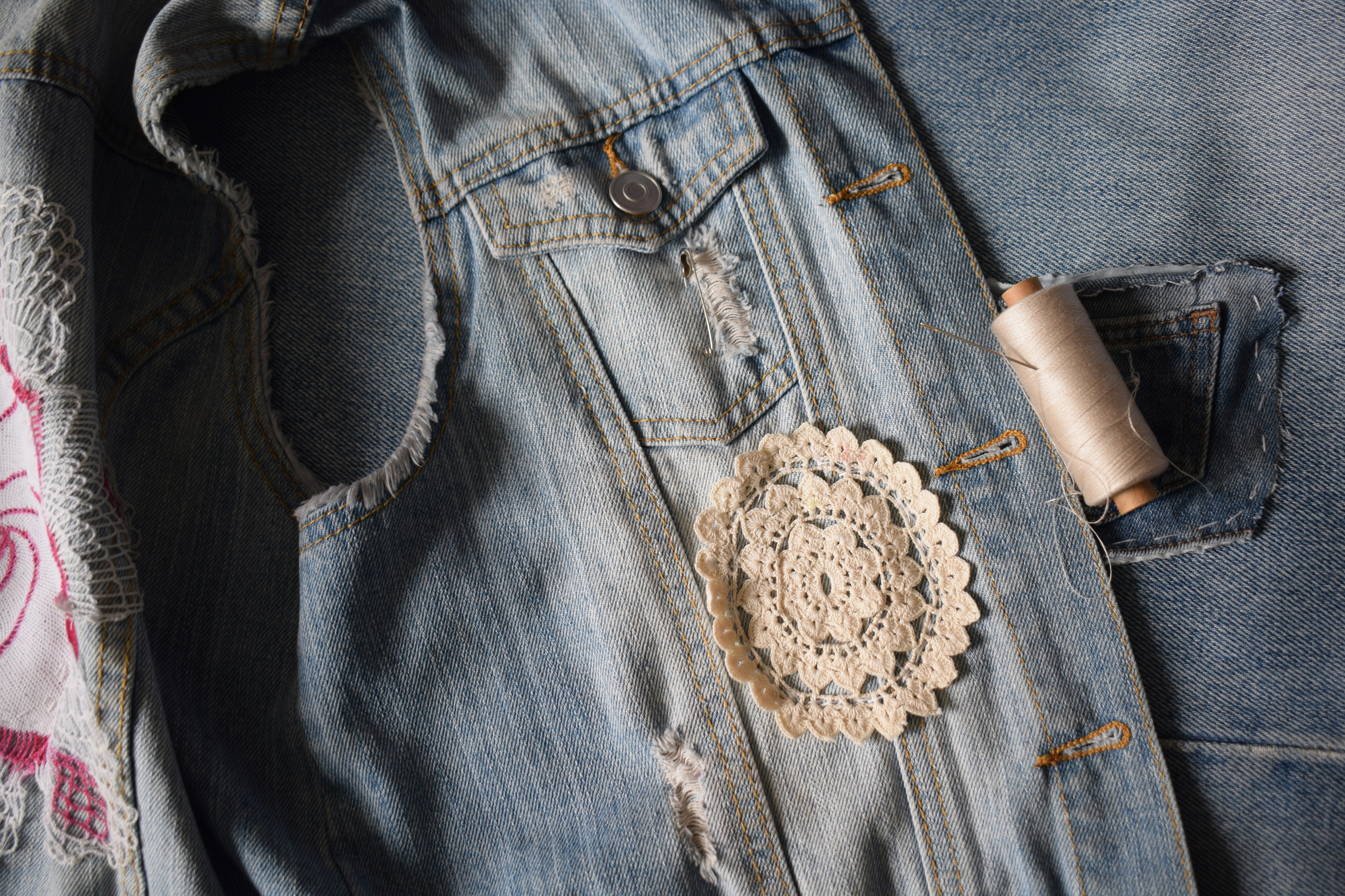 A denim jacket with a crocheted doily and a spool of thread