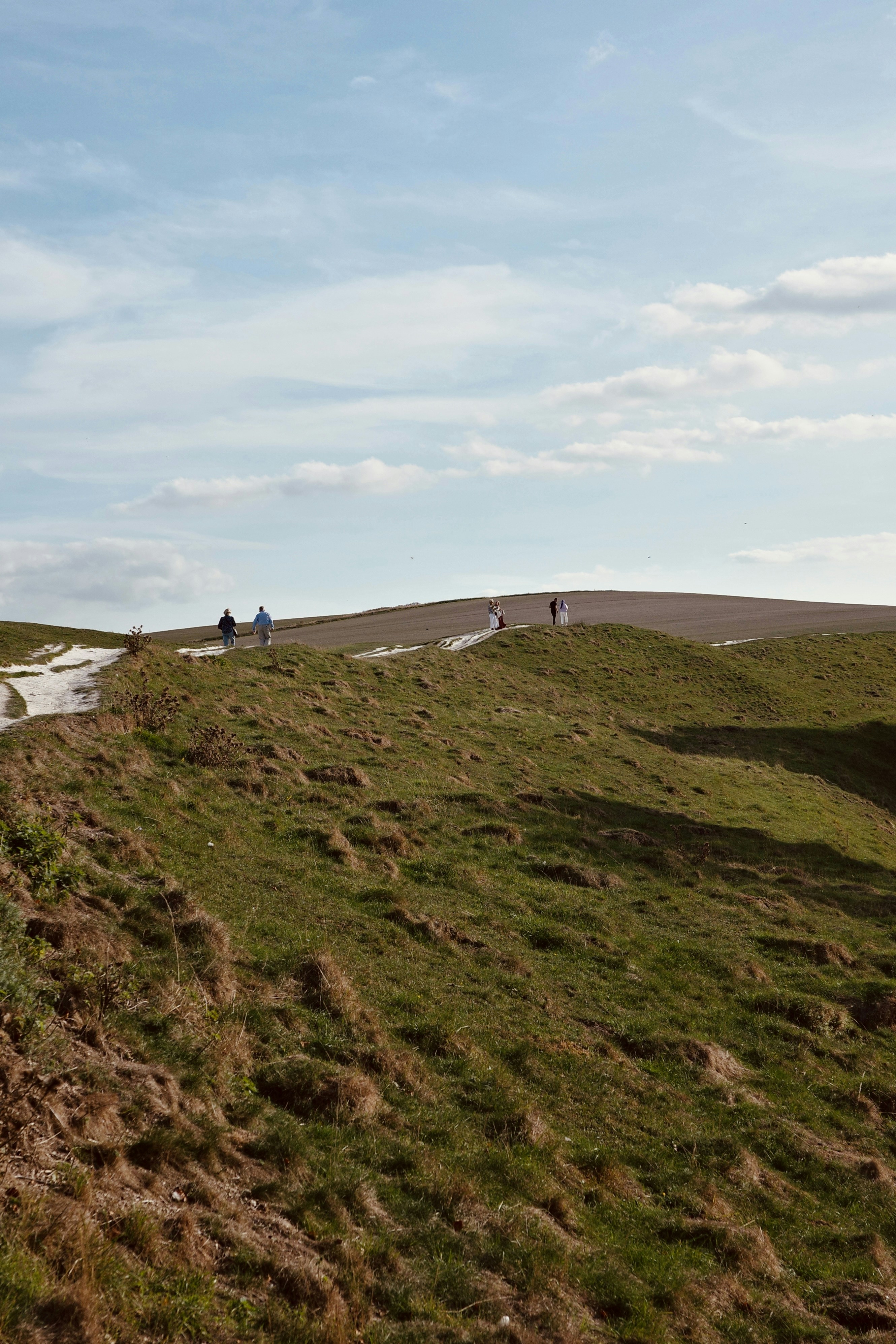 People walking on a grassy chalk hill under a blue sky with clouds