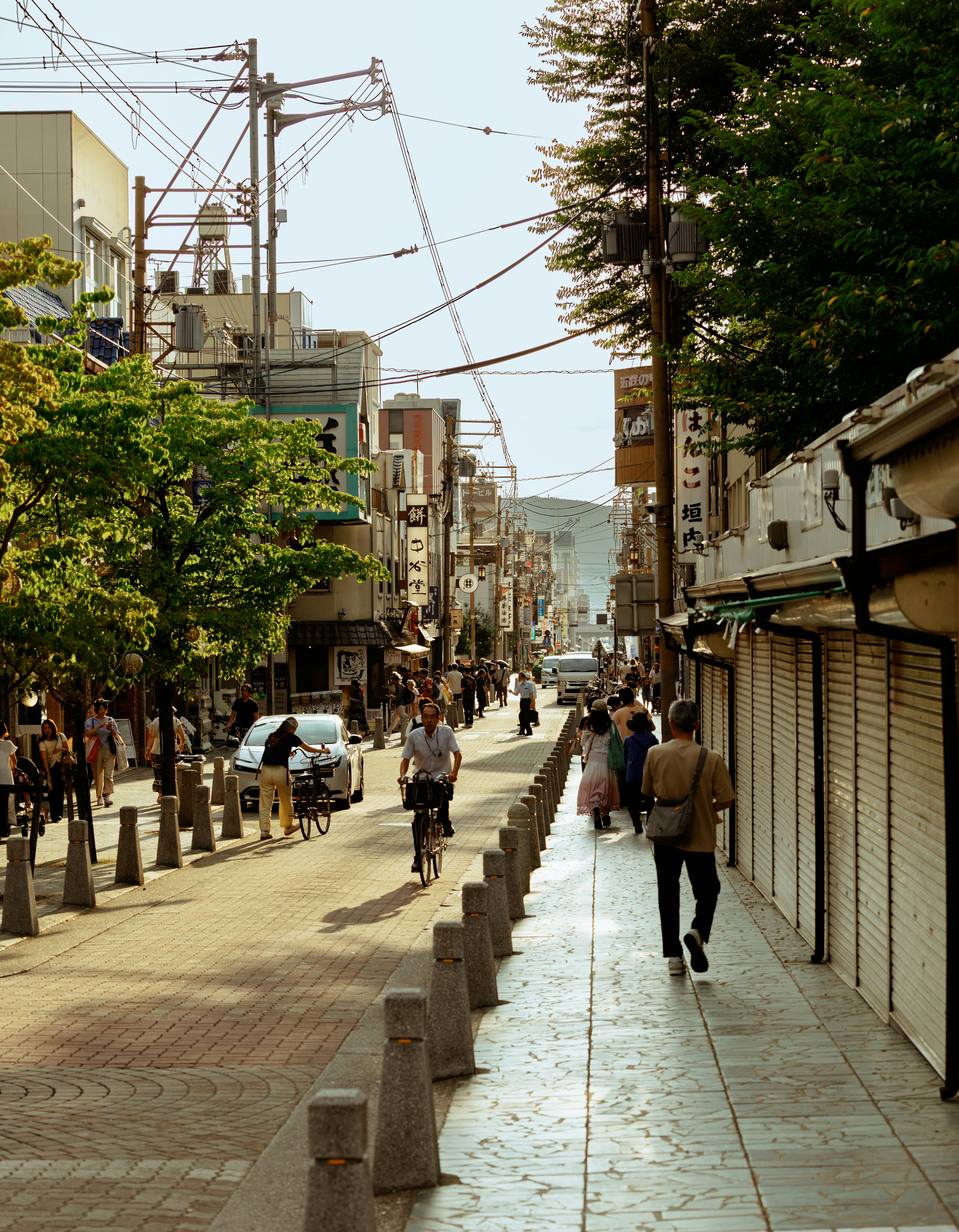 People walking and cycling along a sunlit street in a Japanese town